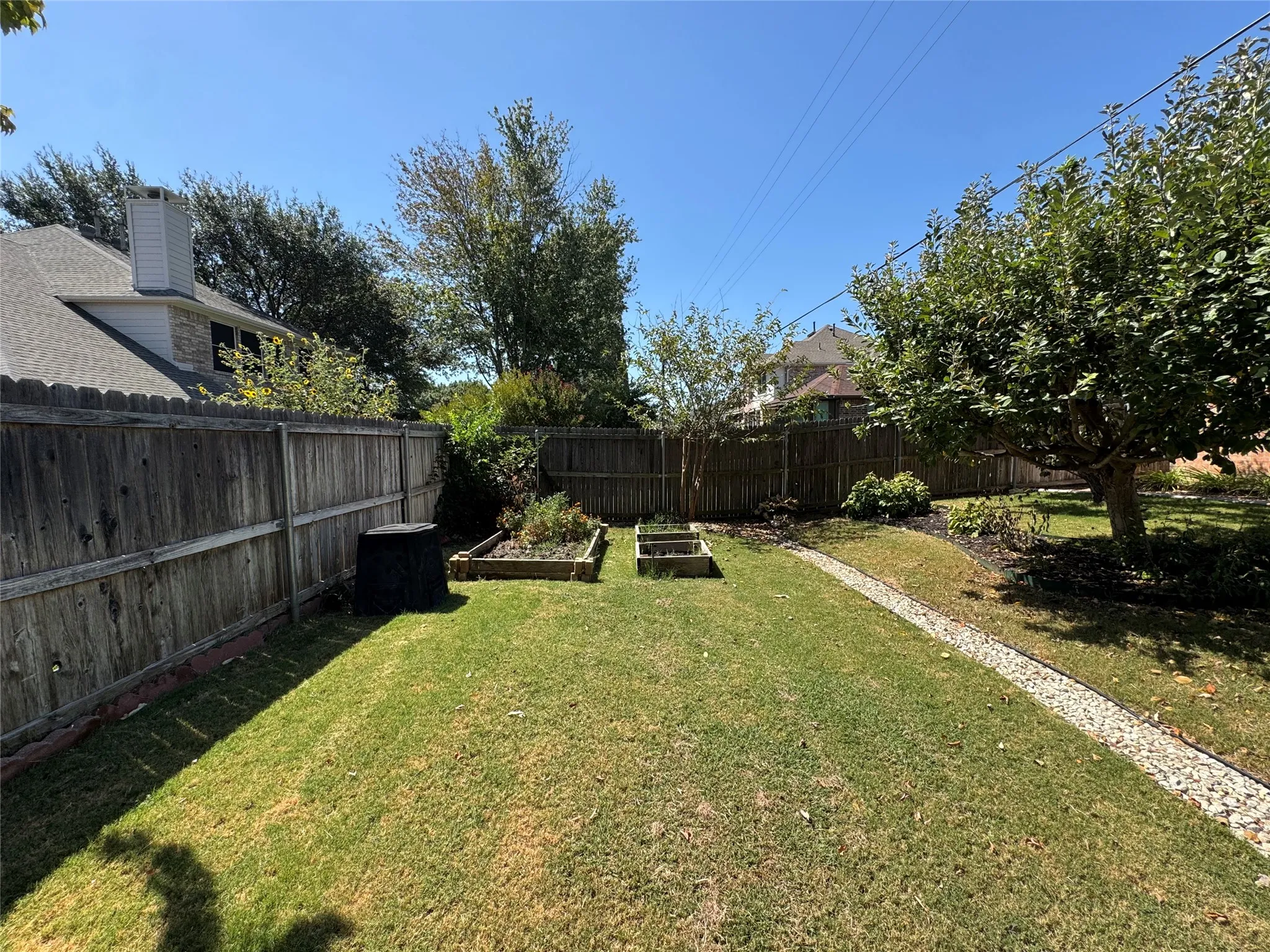 Expansive fenced yard featuring a gravel pathway, mature trees, and two raised garden beds