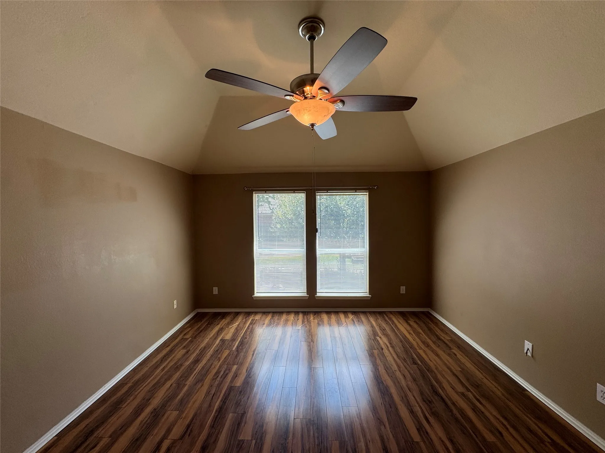 Vaulted ceiling with a ceiling fan light fixture, wood-finish flooring, and two windows