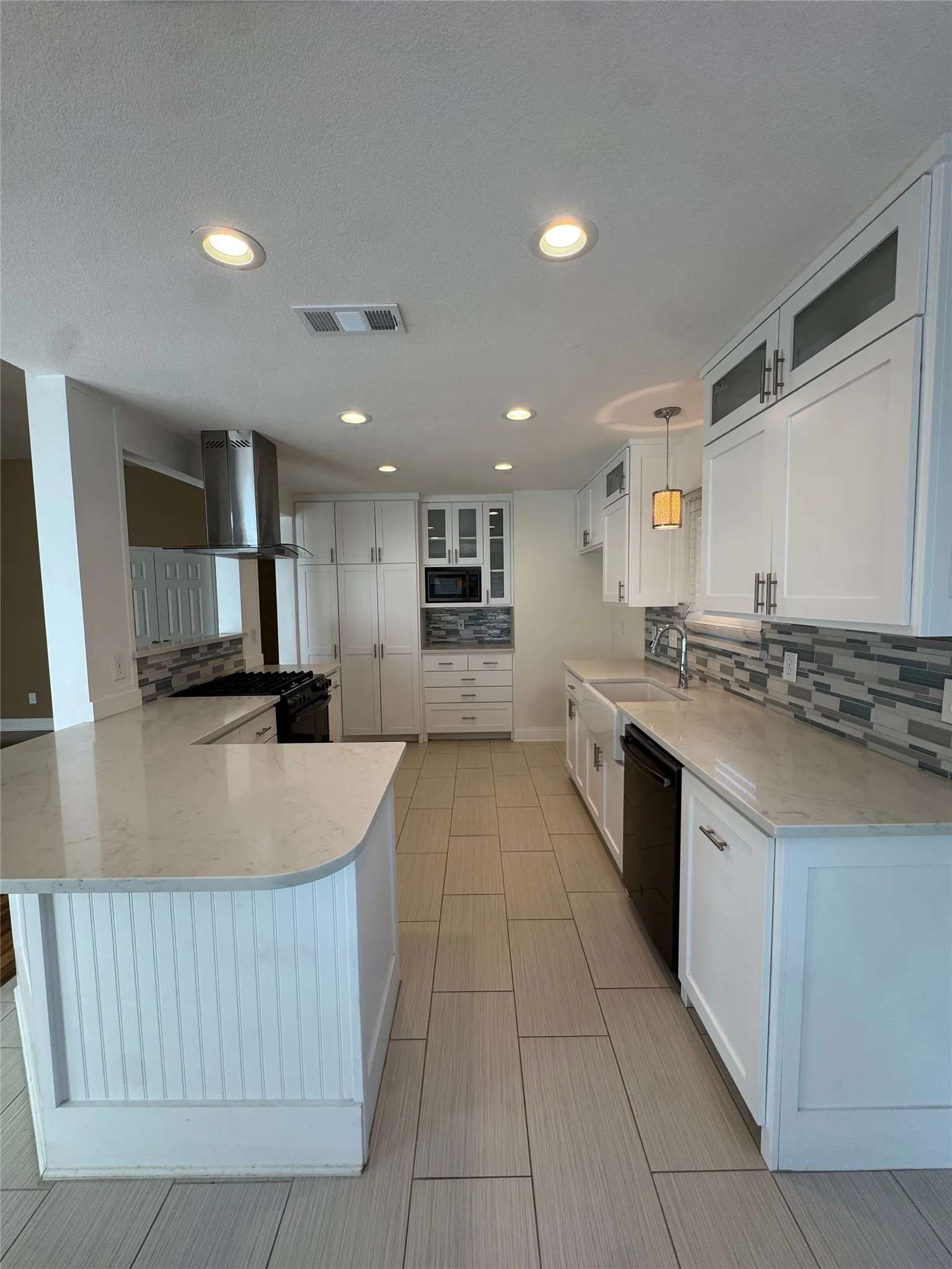 Contemporary kitchen featuring white cabinetry, light-toned countertops, a stainless steel range hood, an integrated microwave, and an undermount sink
