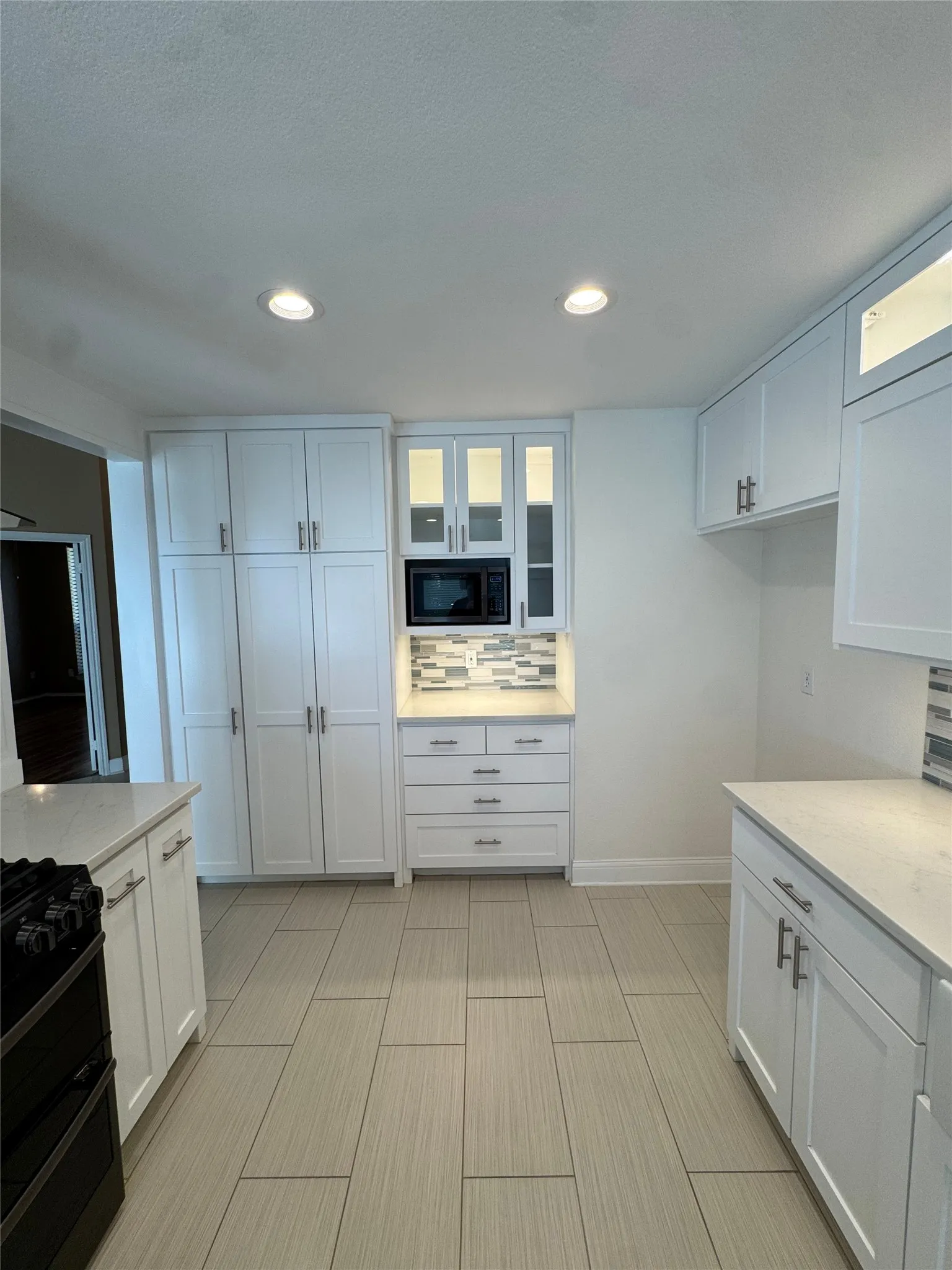 Kitchen featuring white cabinetry, light-toned countertops, a built-in microwave, tile flooring, and recessed ceiling lighting