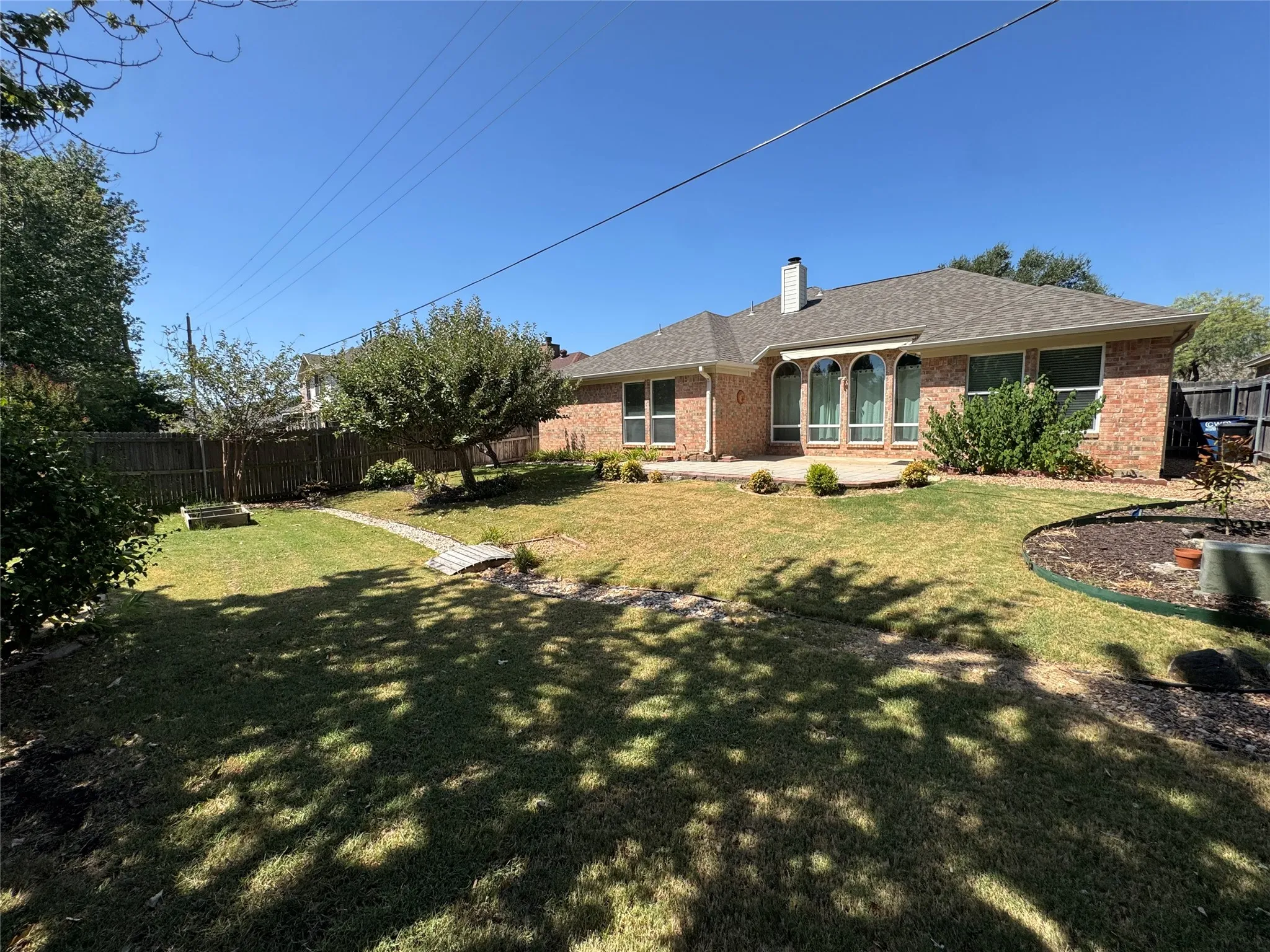 Expansive backyard featuring a manicured lawn, brick exterior, arched windows, patio, and privacy fencing