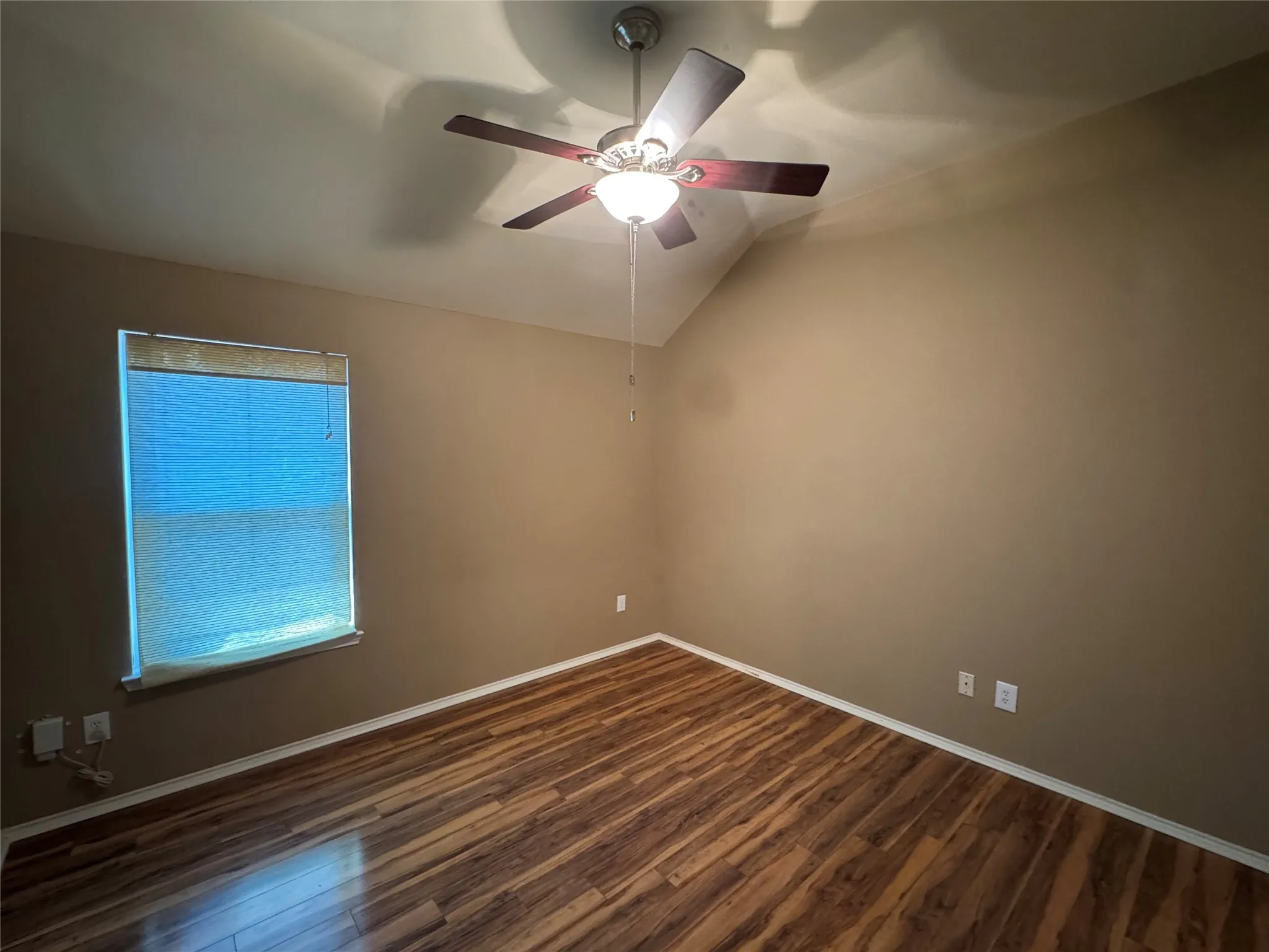 Wood-finish flooring, vaulted ceiling, single window, ceiling fan with integrated lighting, neutral wall tones