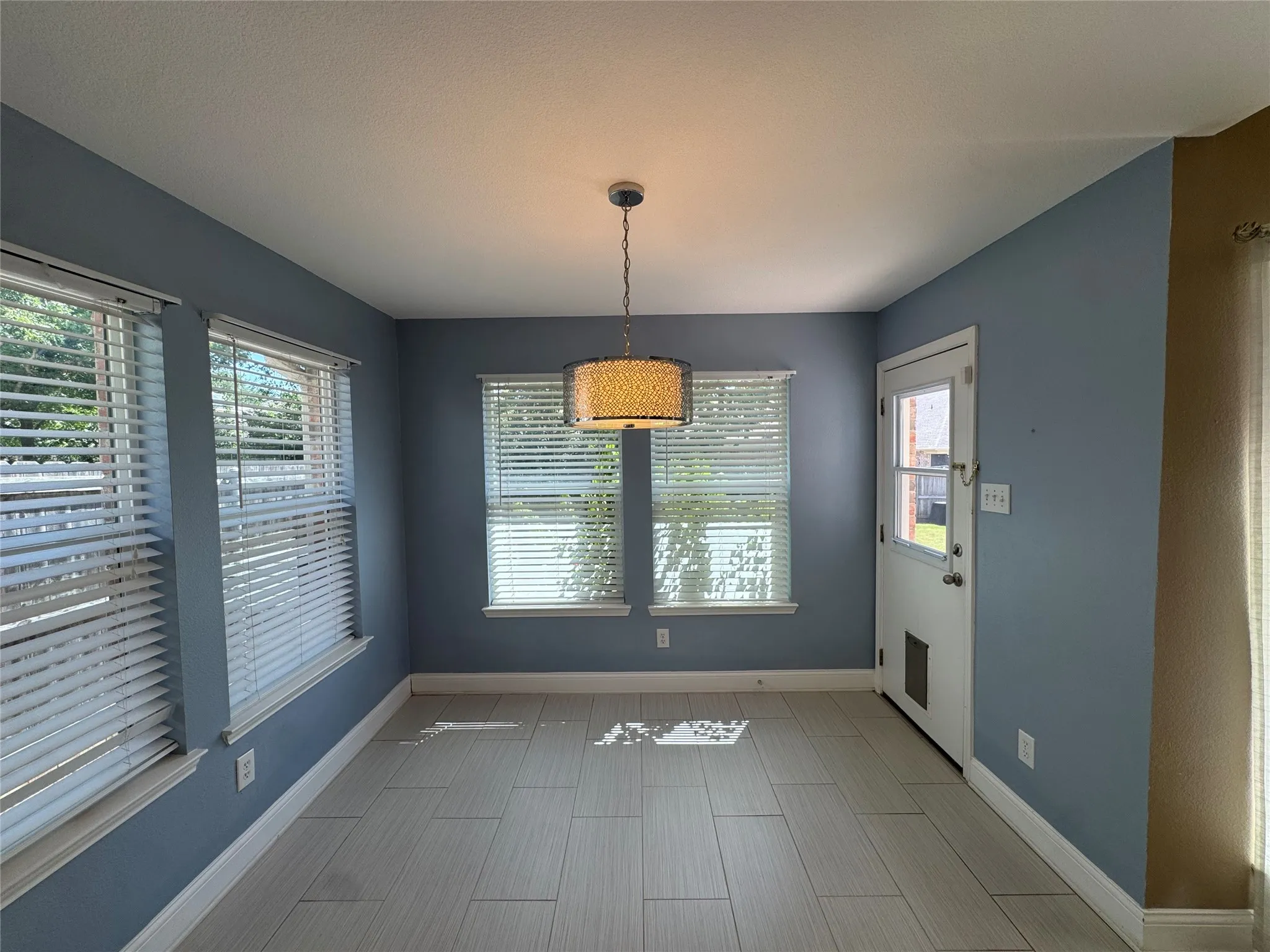 Tile flooring, multiple windows with blinds, a ceiling-mounted light fixture, and a white door with a window