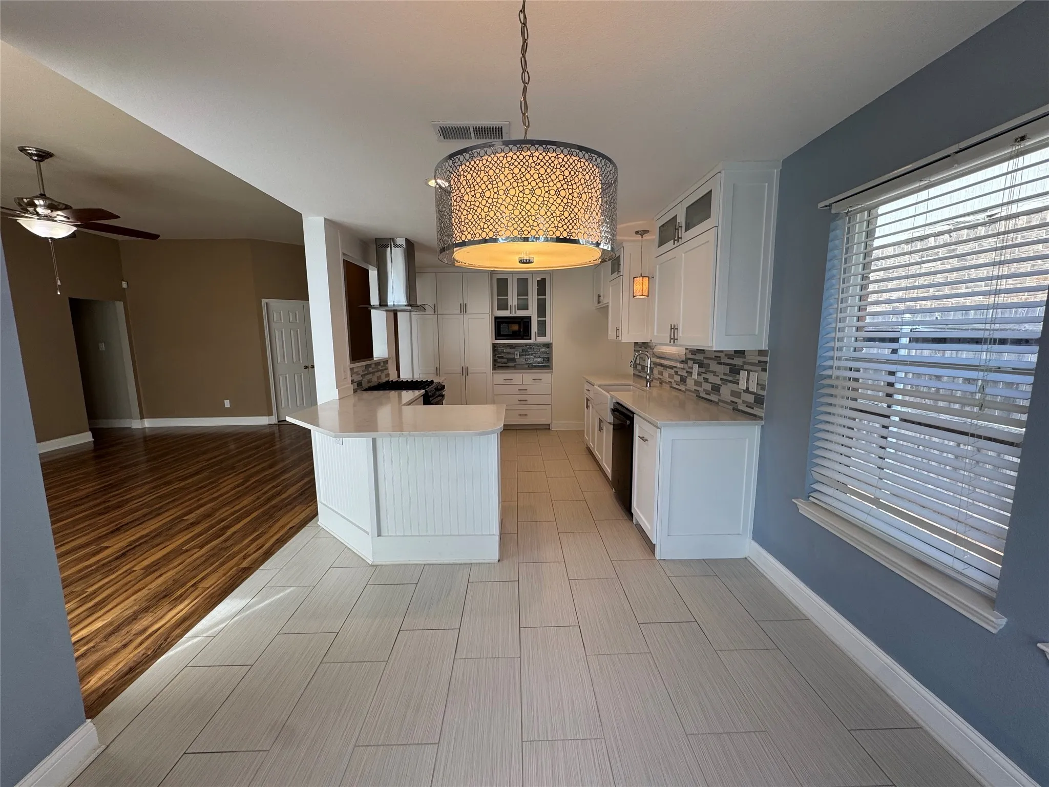 Modern kitchen featuring white cabinetry, light-toned countertops, a geometric patterned backsplash, stainless steel appliances, and a decorative drum pendant light