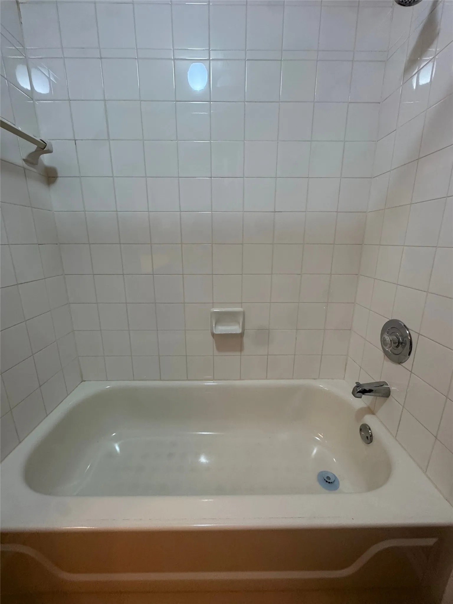 White tiled shower surround with a built-in tub, chrome shower fixtures, and a built-in soap dish