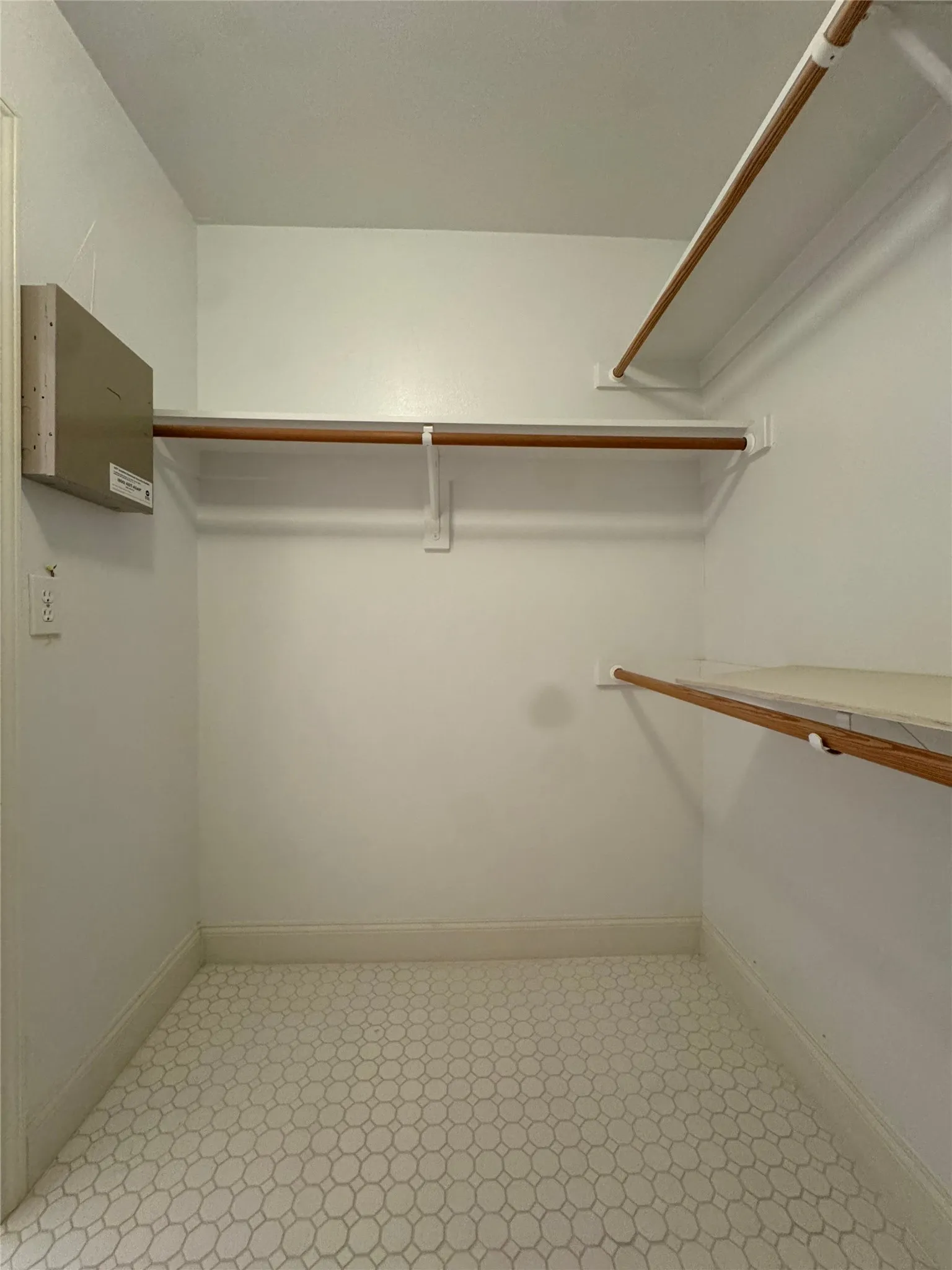 Custom closet system with multiple wooden rods and shelving, complemented by a patterned floor tile