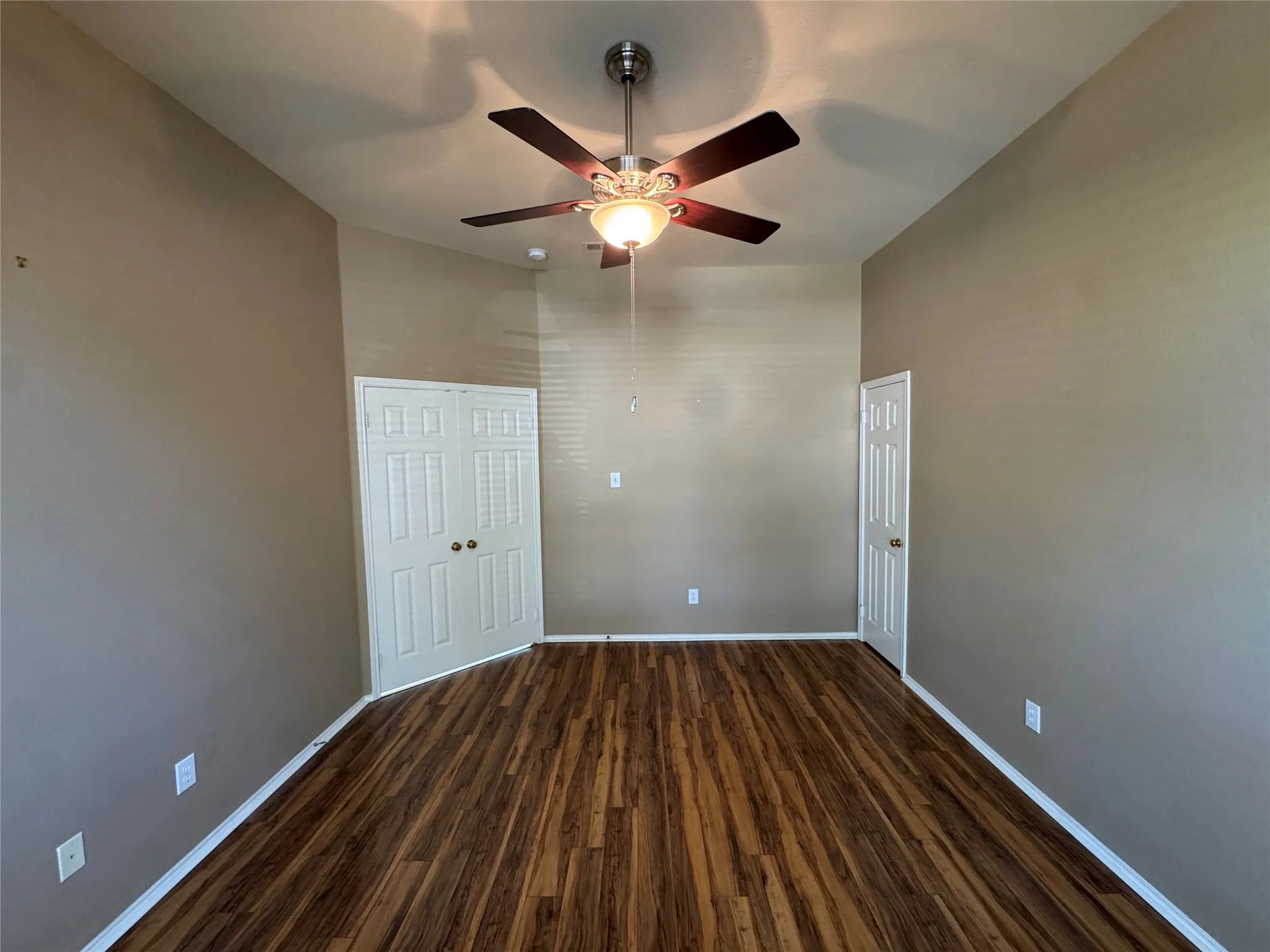 Wood-finish flooring, ceiling fan with integrated lighting, neutral wall tones, and white interior doors
