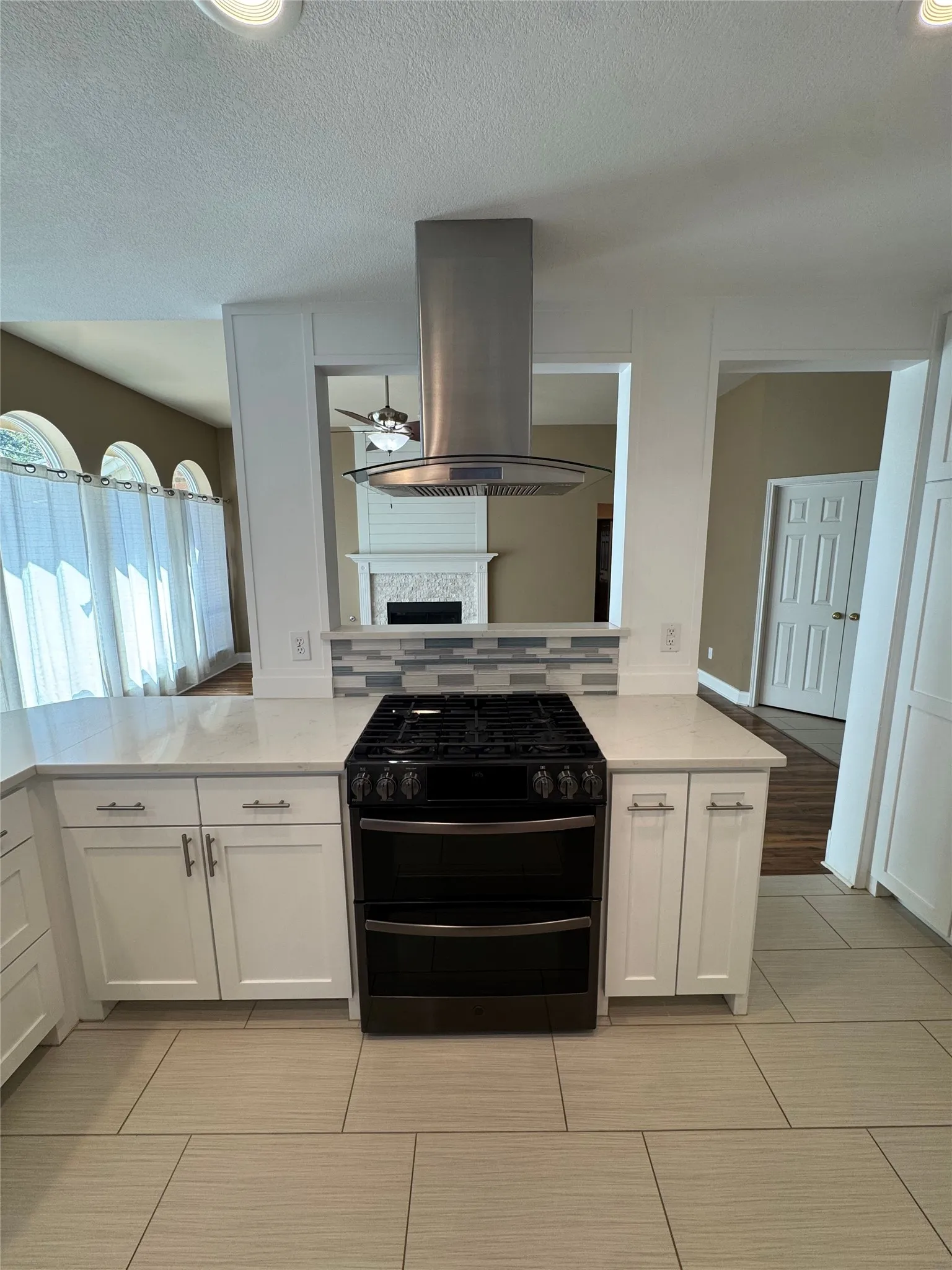 Kitchen featuring a stainless steel range hood, a gas range with a double oven, white shaker-style cabinetry, light-toned countertops, and a tiled backsplash