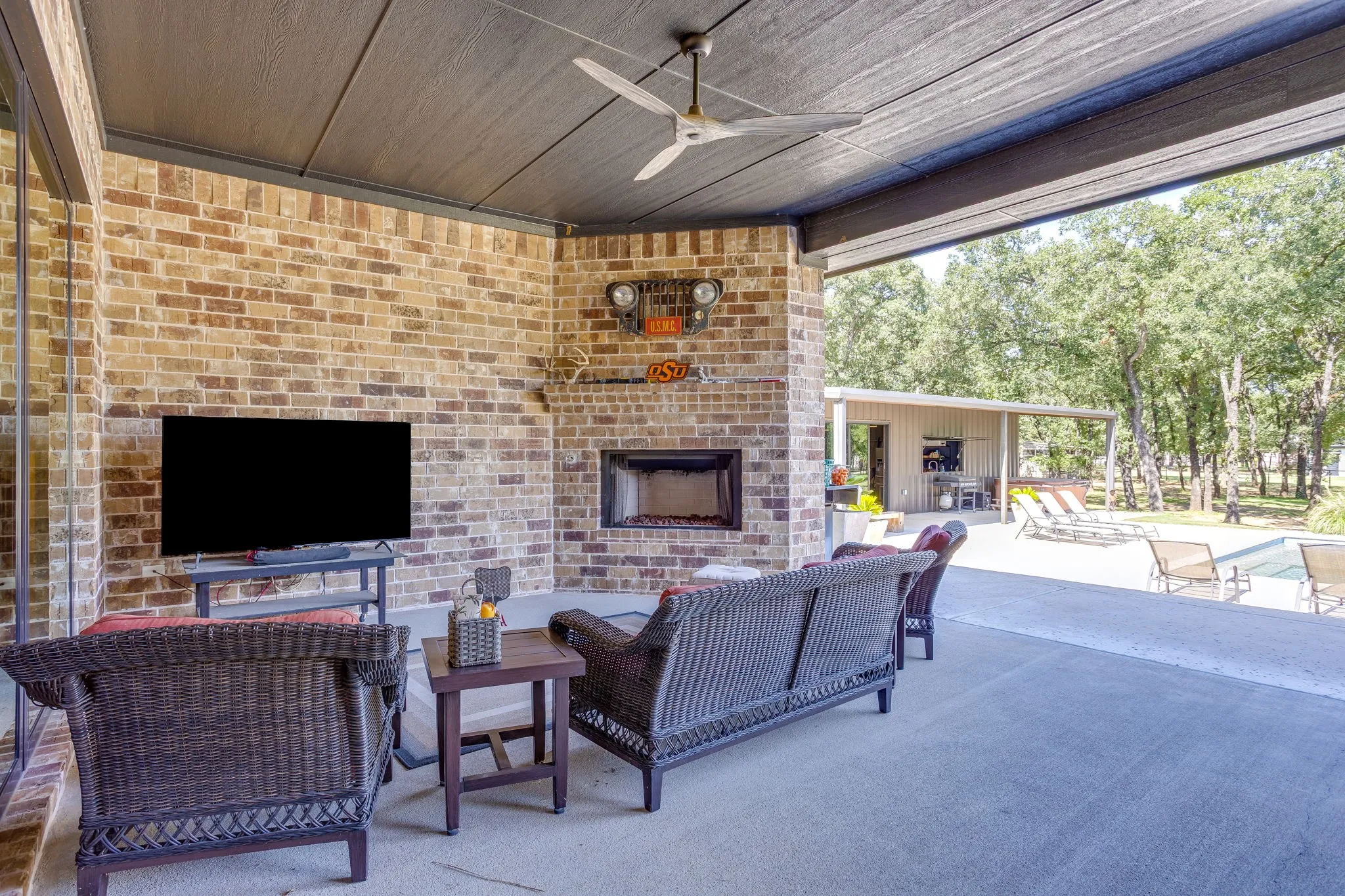 Covered patio featuring a brick fireplace, concrete flooring, and a ceiling fan