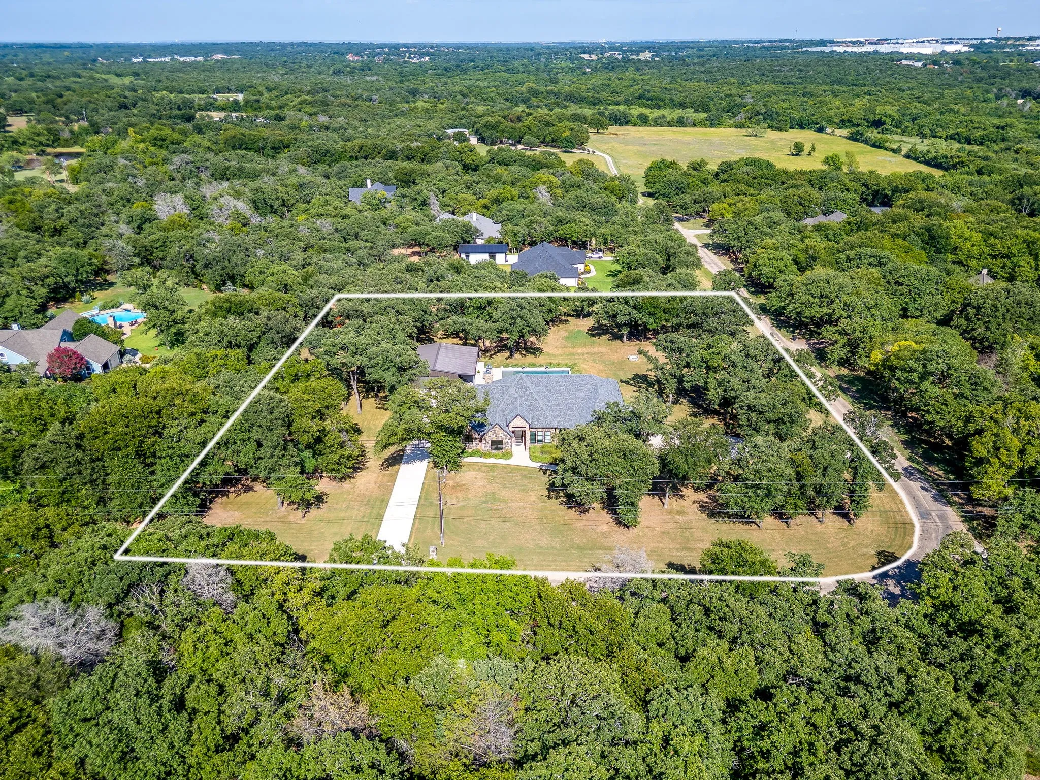 Expansive lot with mature trees, a long driveway, and a visible roofline