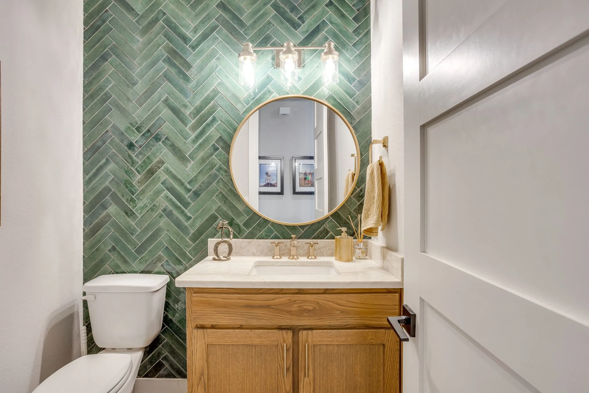 Powder bath featuring herringbone tile accent wall, wood-finish vanity with built-in storage, undermount sink, countertop, and a round wall-mounted mirror