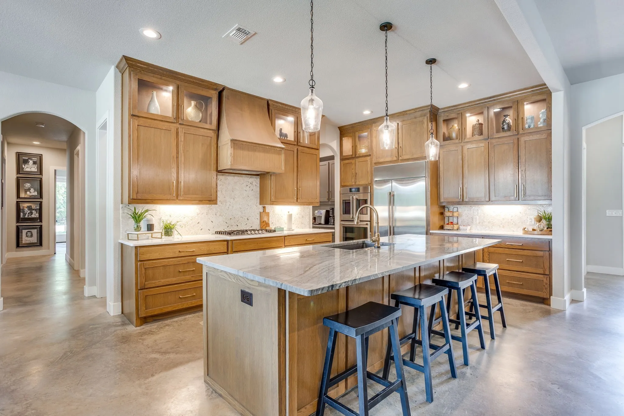 Expansive kitchen featuring wood cabinetry, stainless steel appliances, a large center island with stone countertops, and pendant lighting