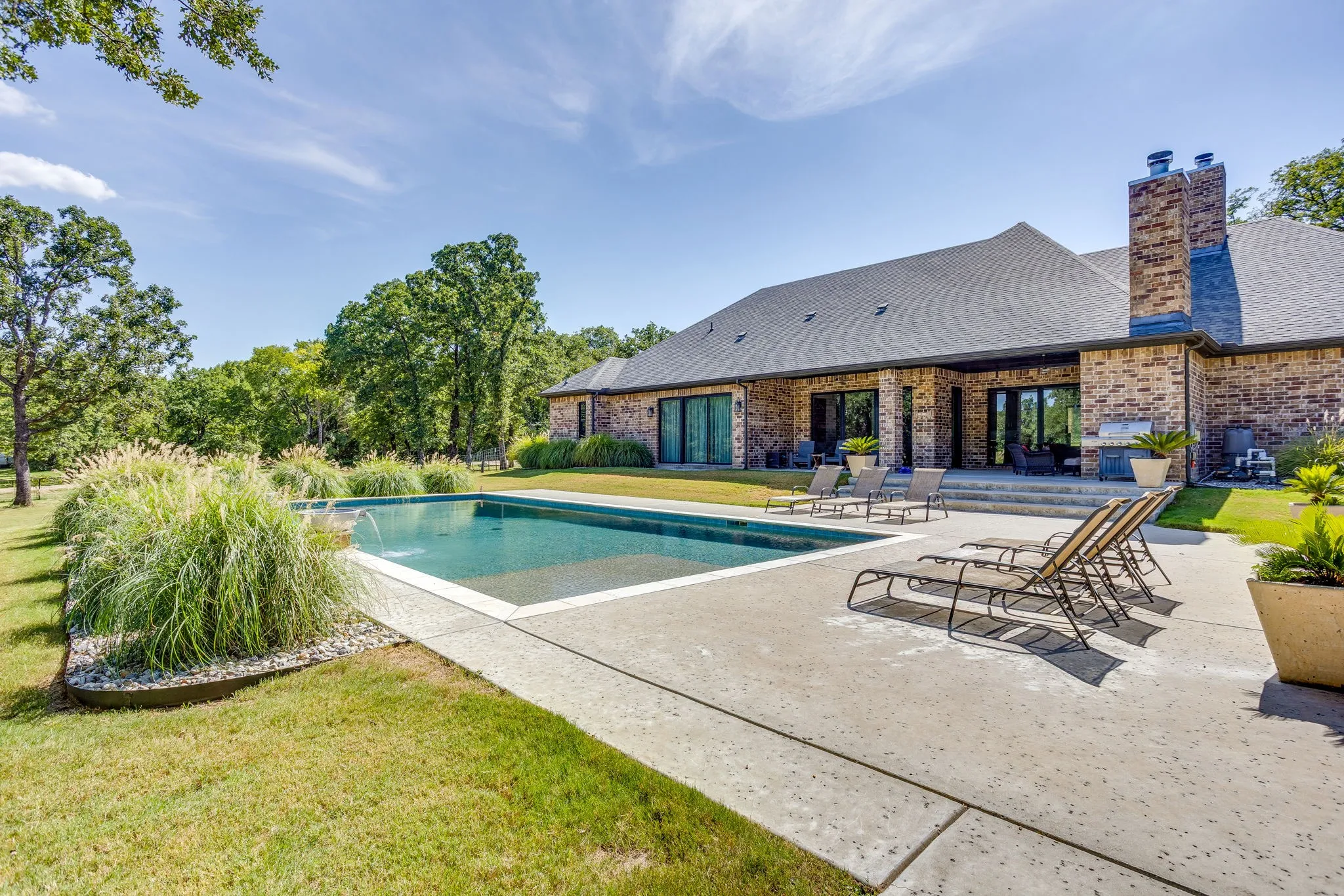 Private backyard featuring an in-ground swimming pool, stone patio, brick exterior, and multiple sliding glass doors