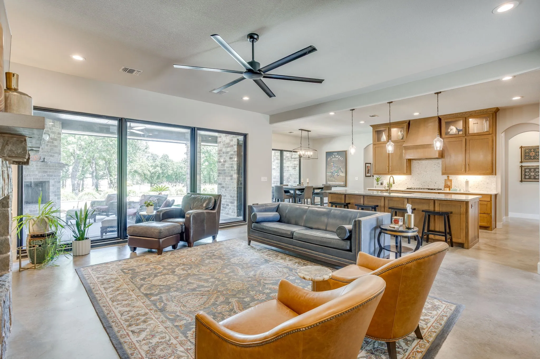 Expansive living area featuring a stone fireplace, large format sliding glass doors, a ceiling fan, recessed lighting, and polished concrete flooring