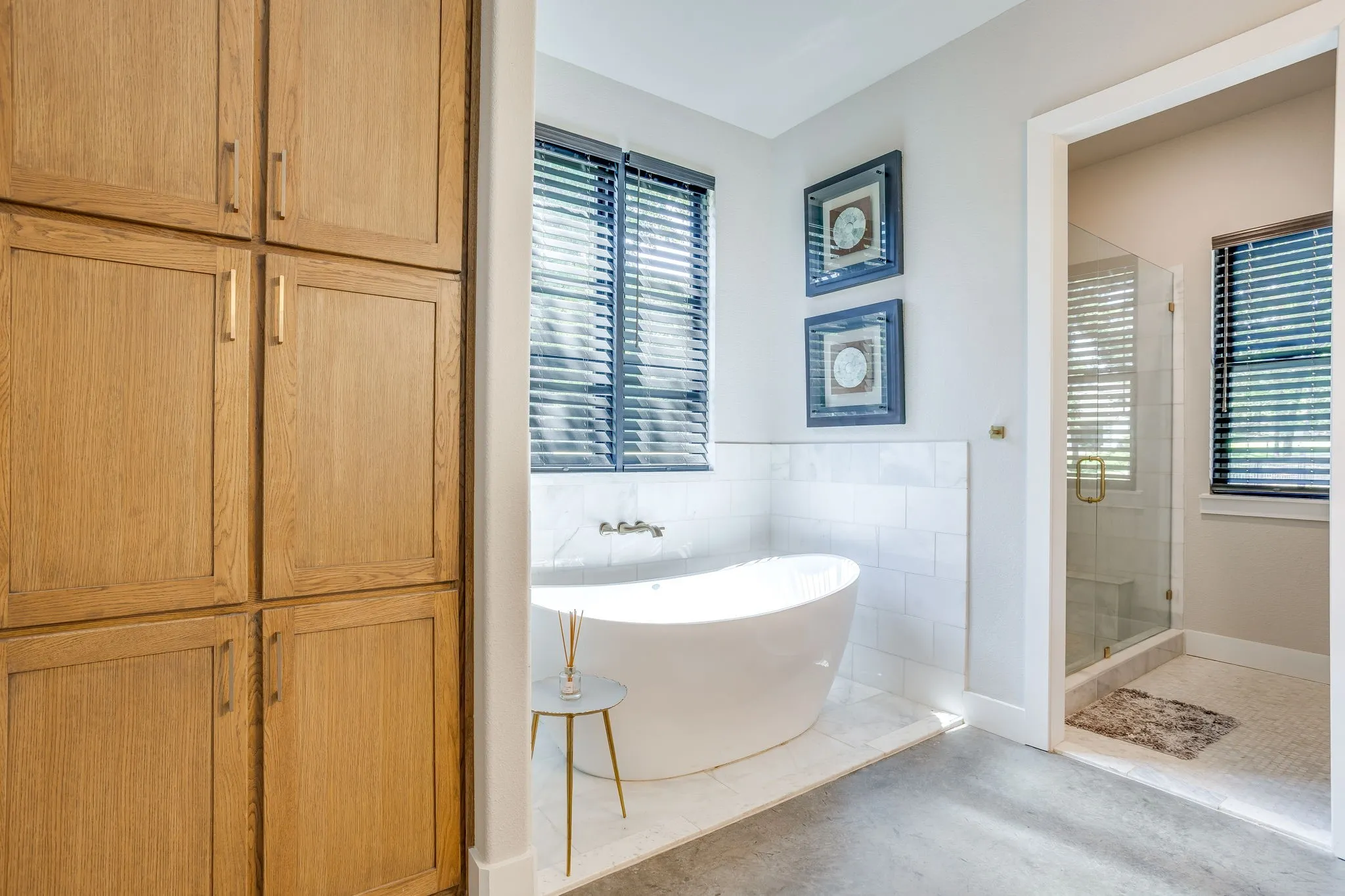 Freestanding soaking tub with wall-mounted brass fixtures, white subway tile wainscoting, and large wood-finish built-in cabinetry