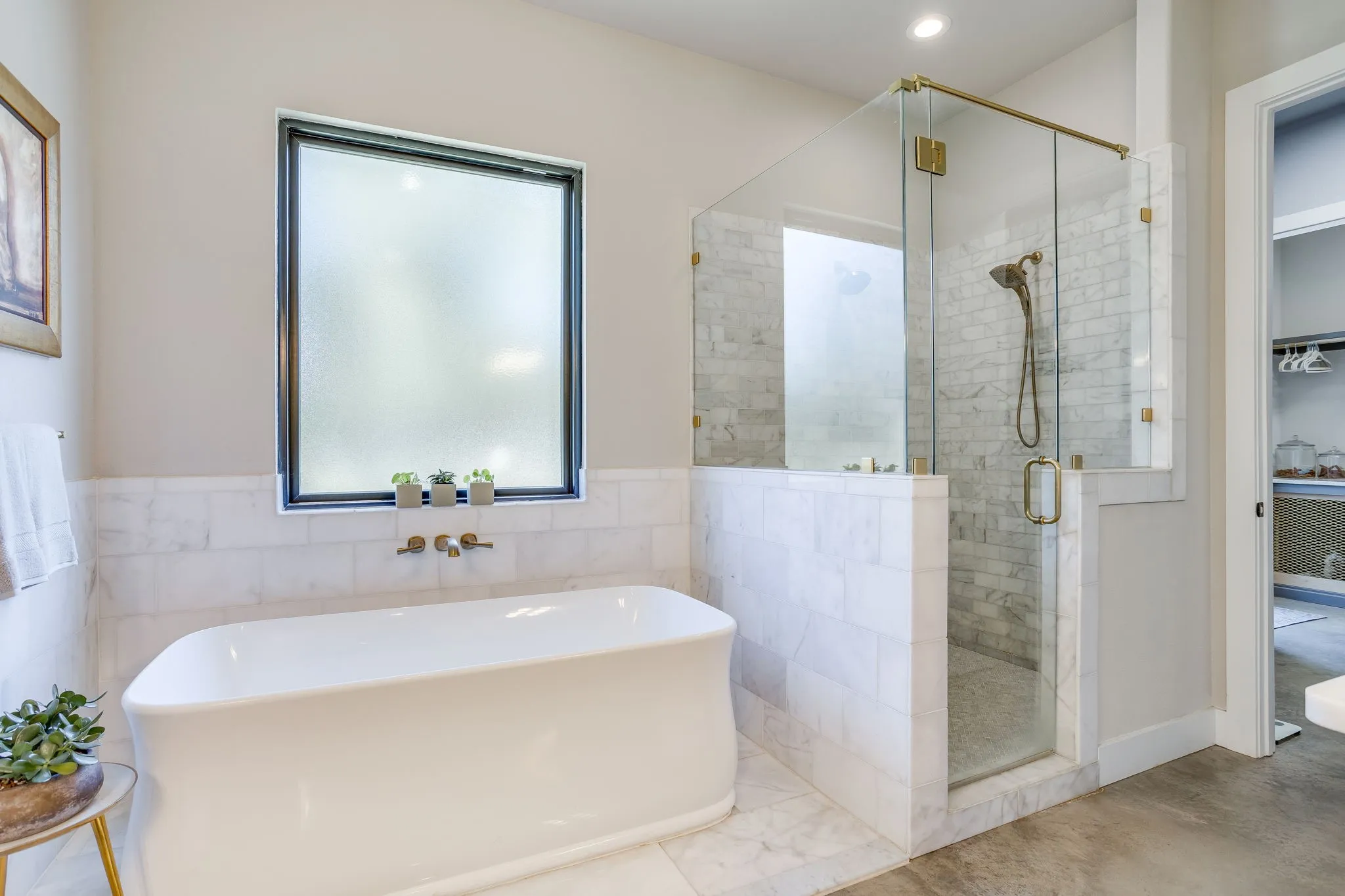 Freestanding soaking tub with wall-mounted brass-finish faucet, walk-in shower with glass enclosure, large format tile walls, and a separate water closet