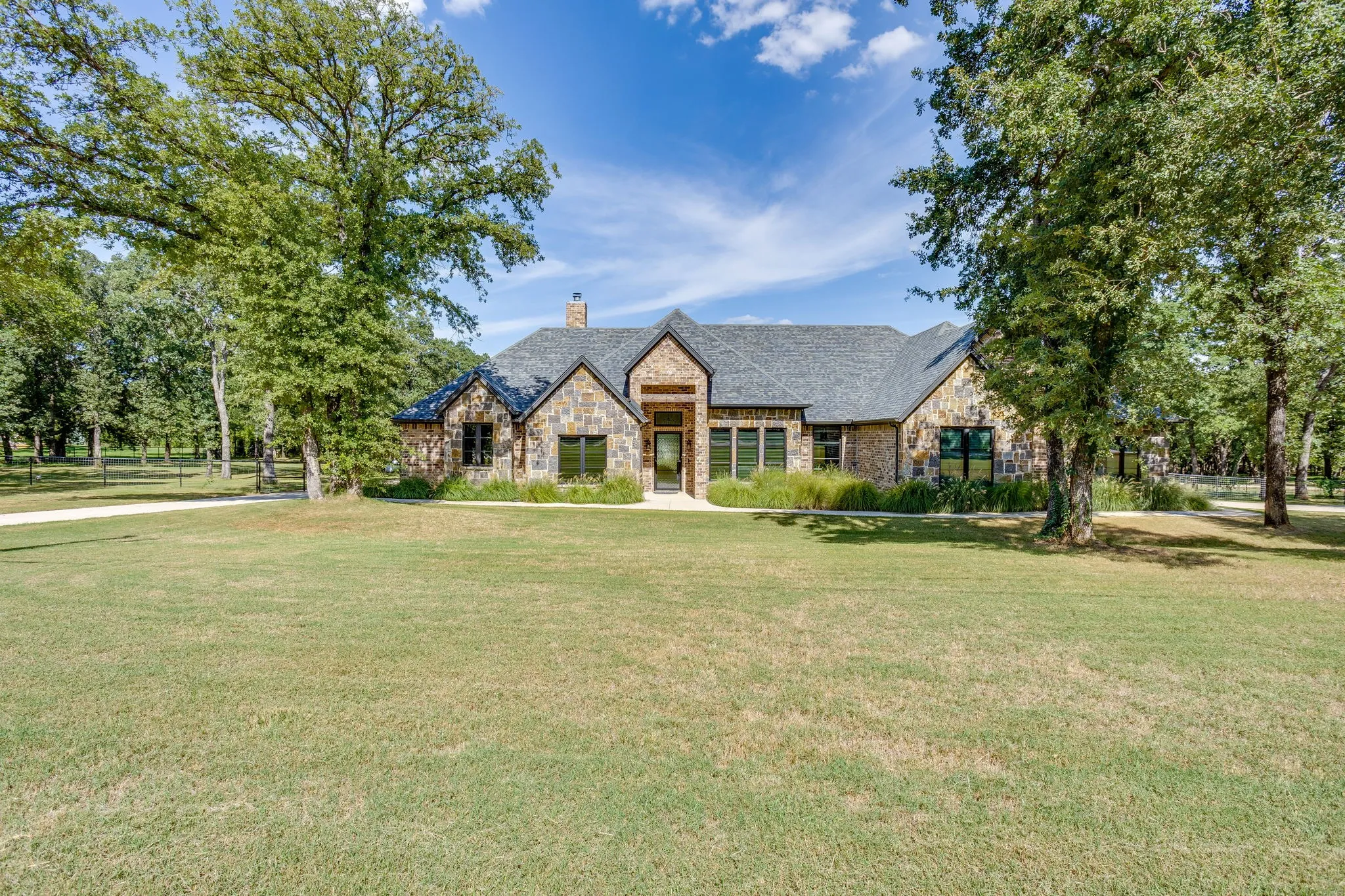 Stone & brick residence featuring a prominent front lawn, mature trees, and a composition shingle roof