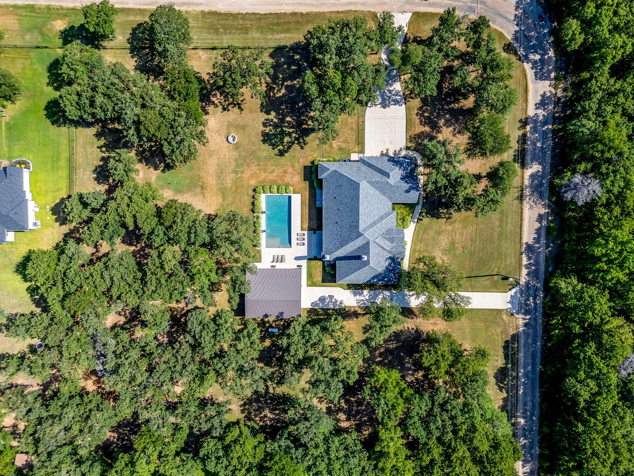 Expansive property featuring a rectangular pool, mature trees, concrete driveway, and a composition shingle roof