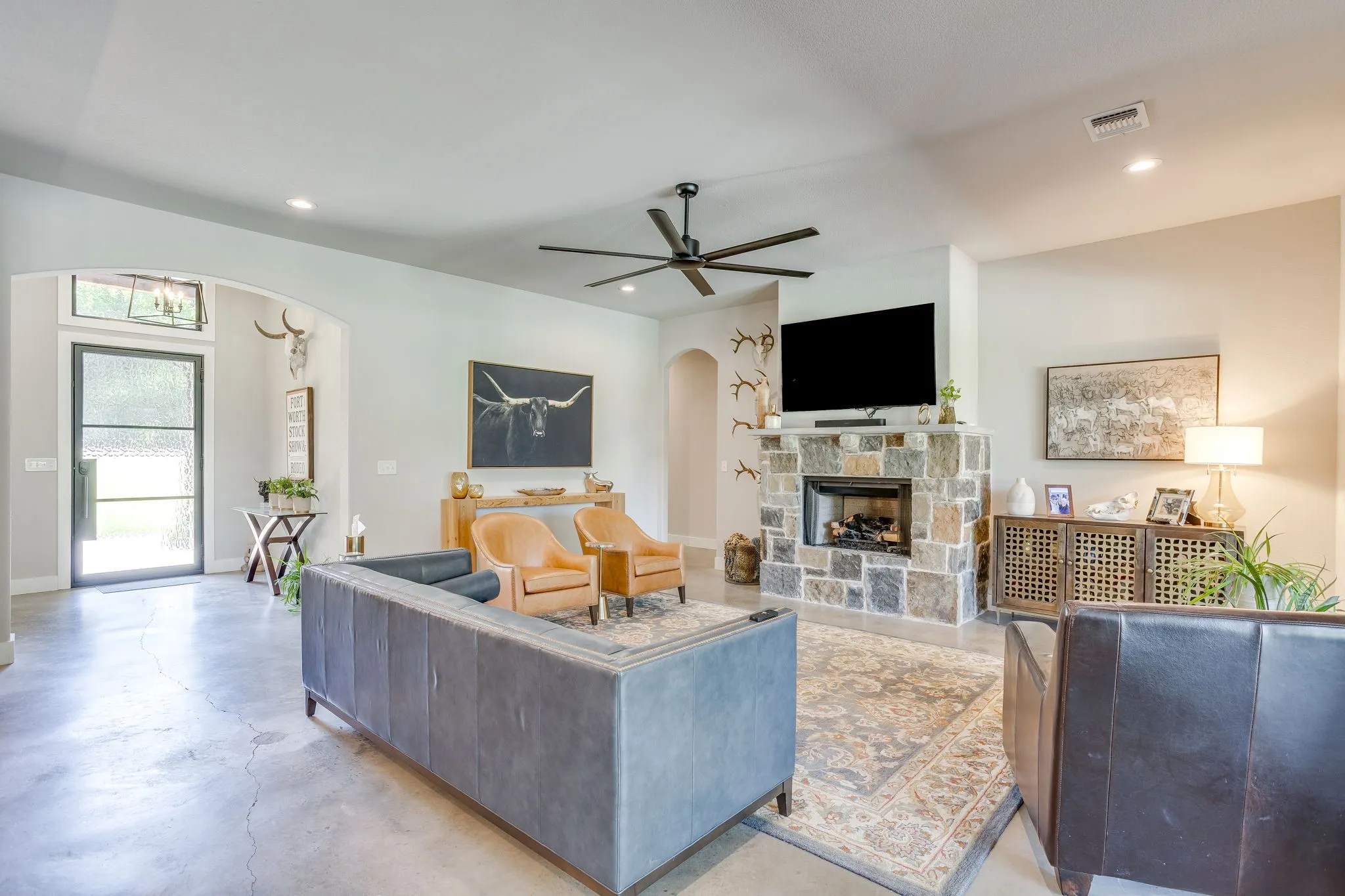Stone fireplace with a built-in propane firebox, concrete flooring, and a ceiling fan