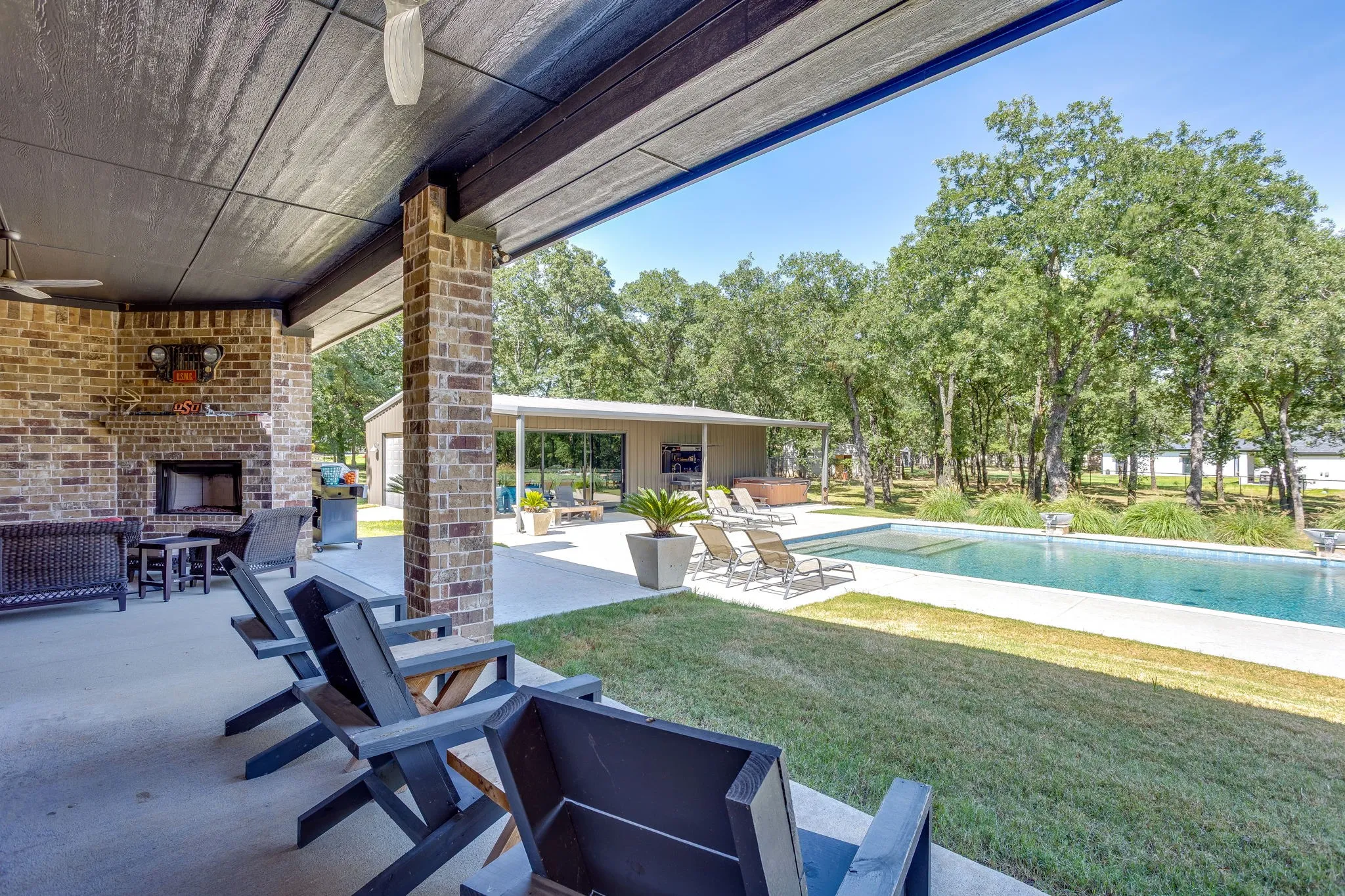Covered patio featuring a brick fireplace, concrete flooring, and ceiling fan with view of pool