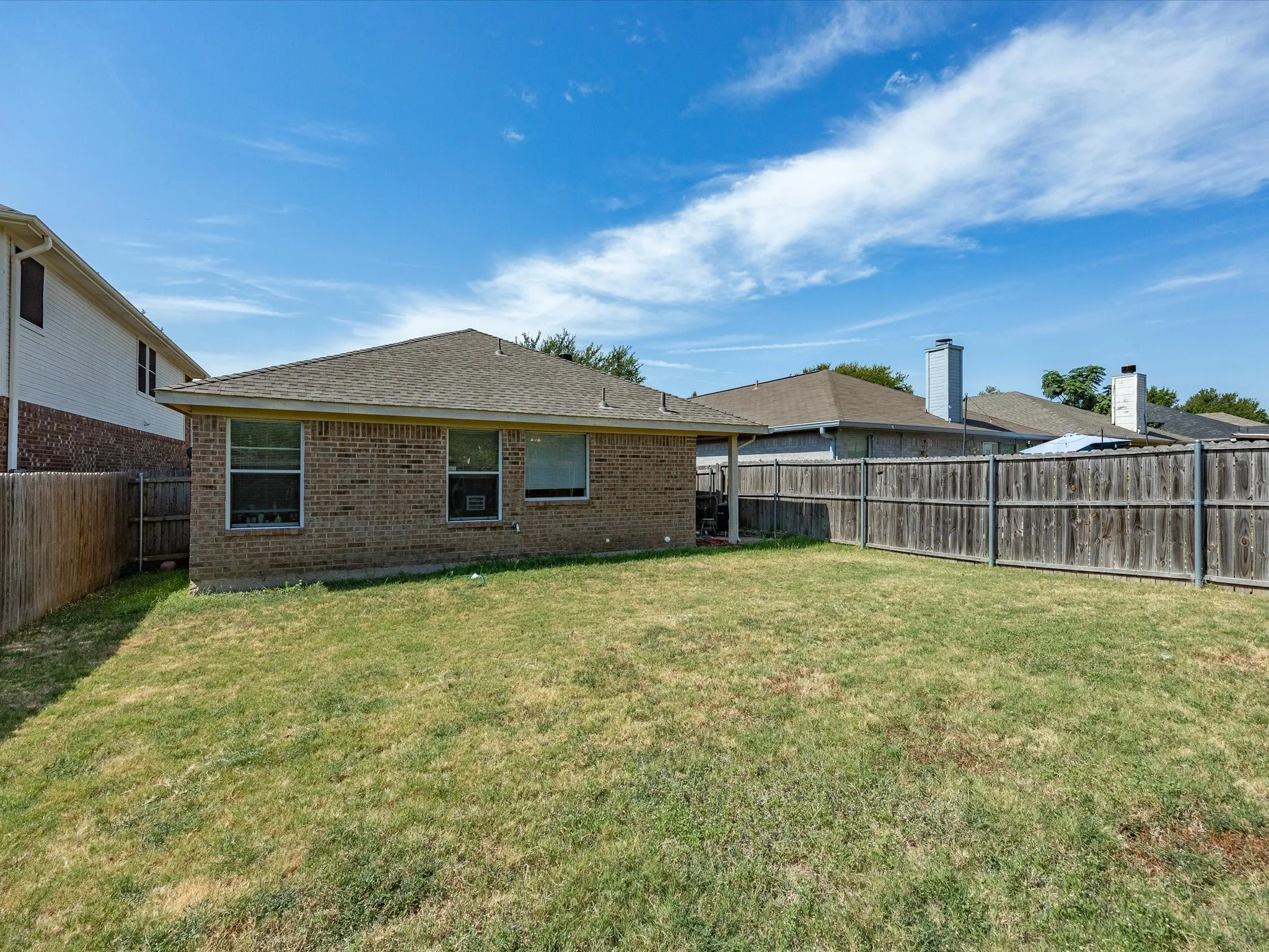 Spacious backyard featuring a wood fence perimeter and a brick exterior with multiple windows