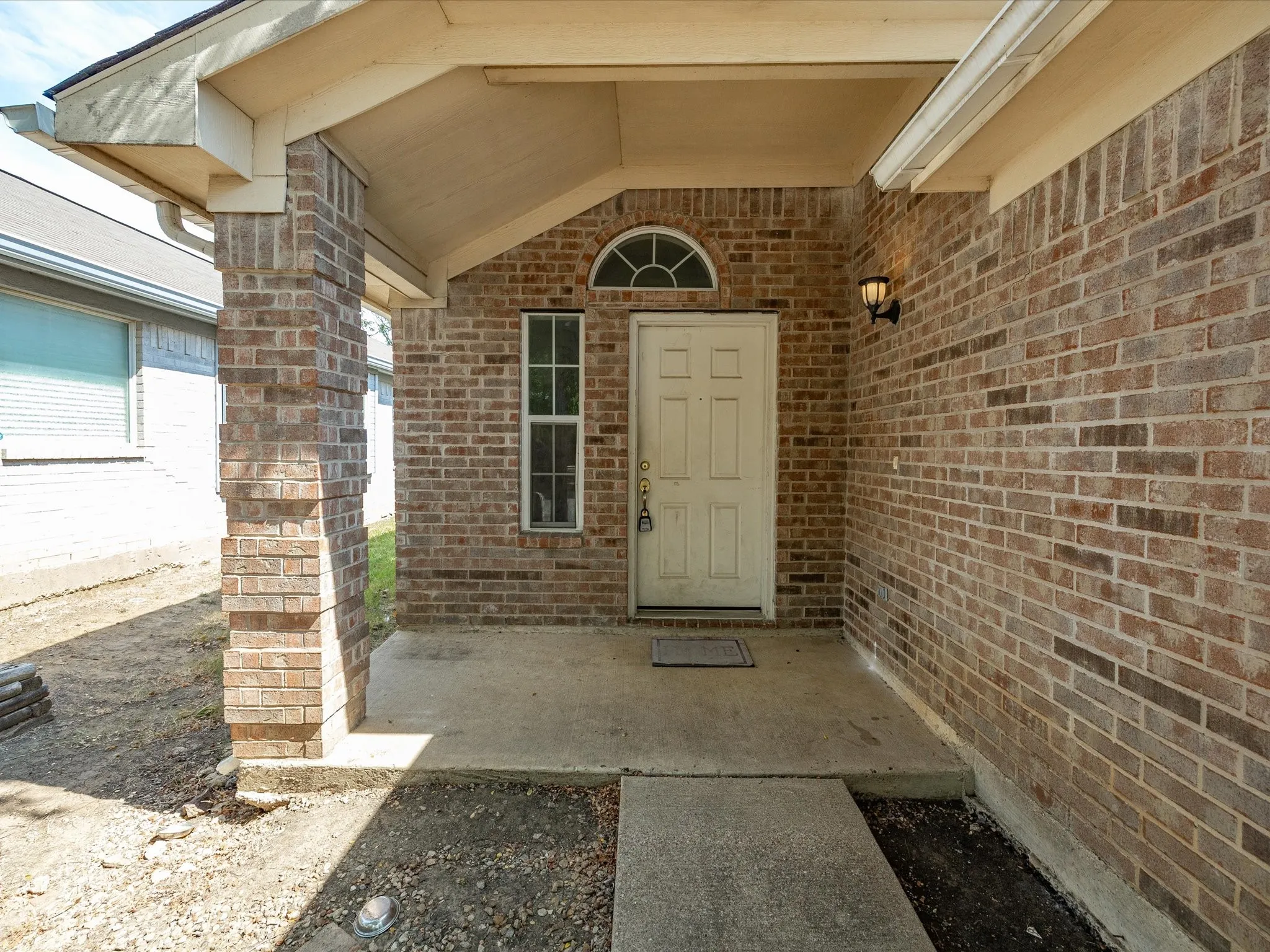 Brick exterior with a covered entry, concrete porch, and arched transom window