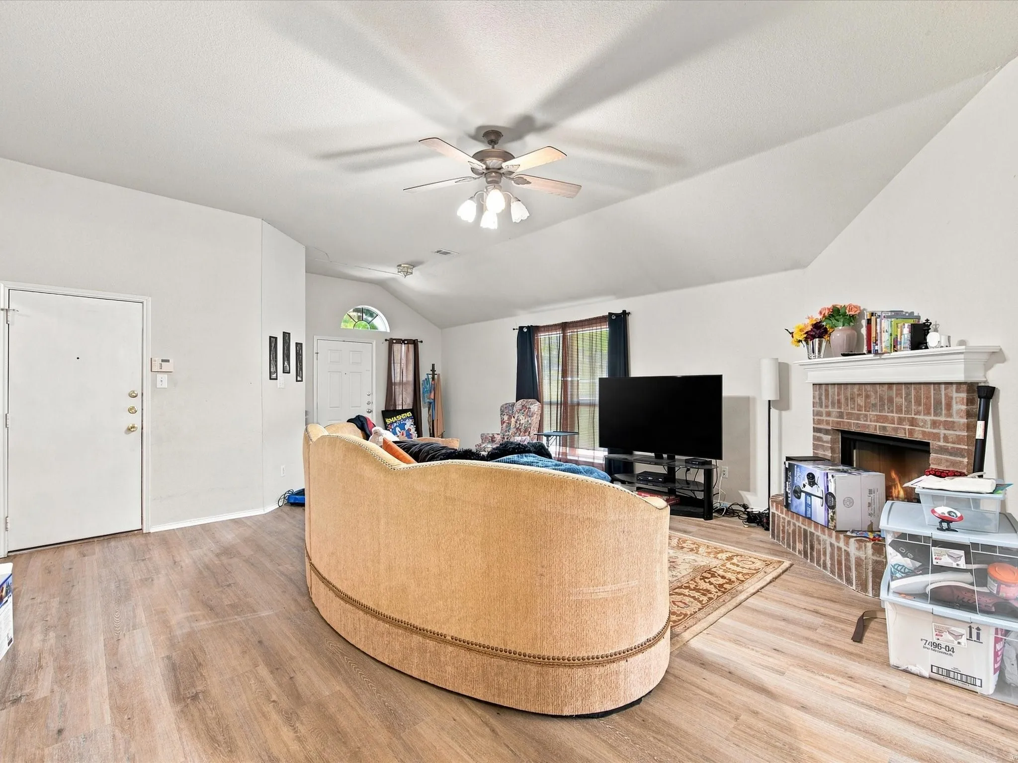 Vaulted ceiling featuring a ceiling fan, wood-finish flooring, and a brick fireplace with a white mantel
