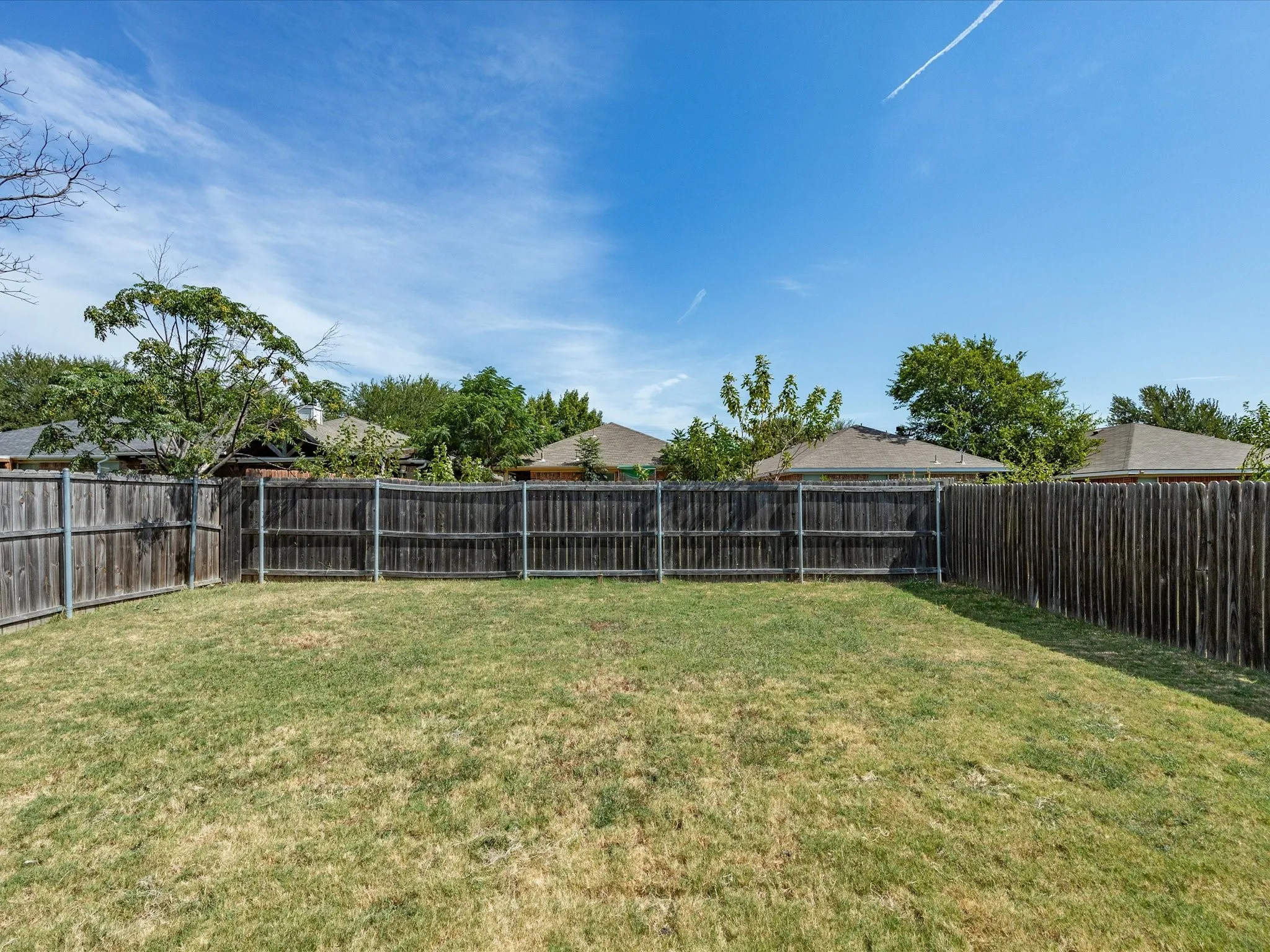 Expansive backyard featuring a natural grass lawn and wood privacy fencing
