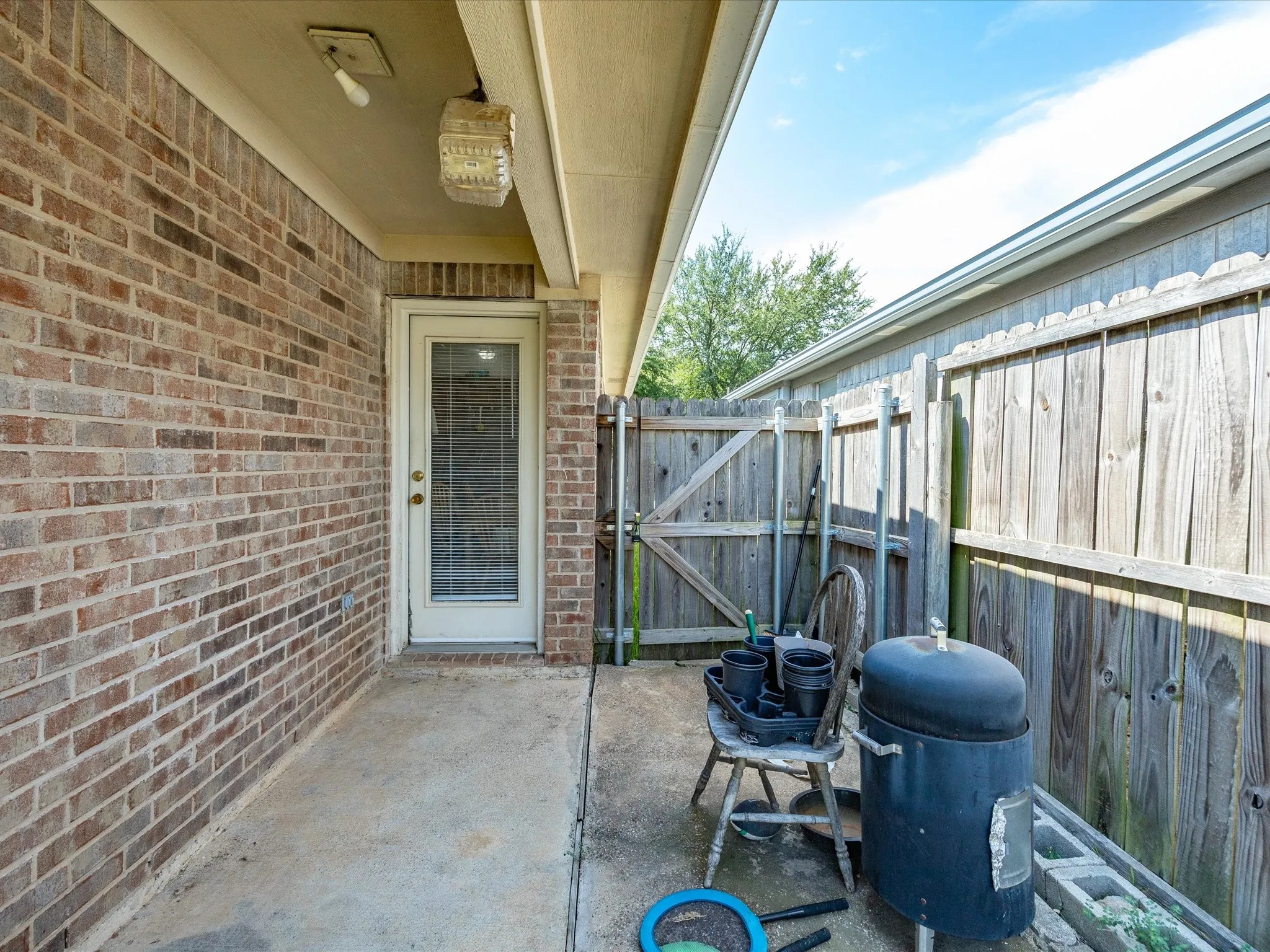 Brick exterior with concrete patio, featuring an exterior door with glass insert, privacy fencing, and an overhead awning