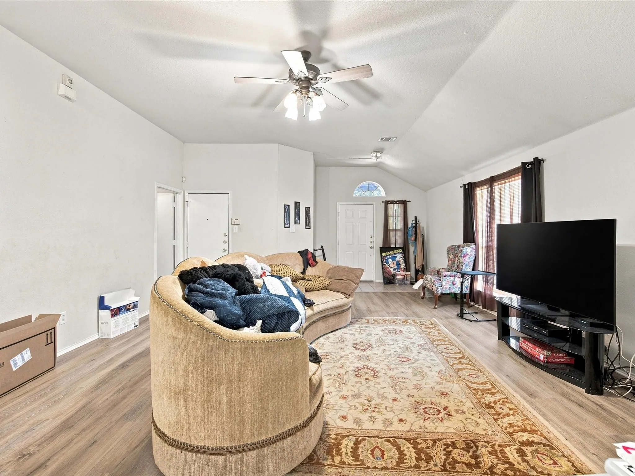 Vaulted ceiling with an attached ceiling fan, wood-finish flooring, and large windows with privacy drapes