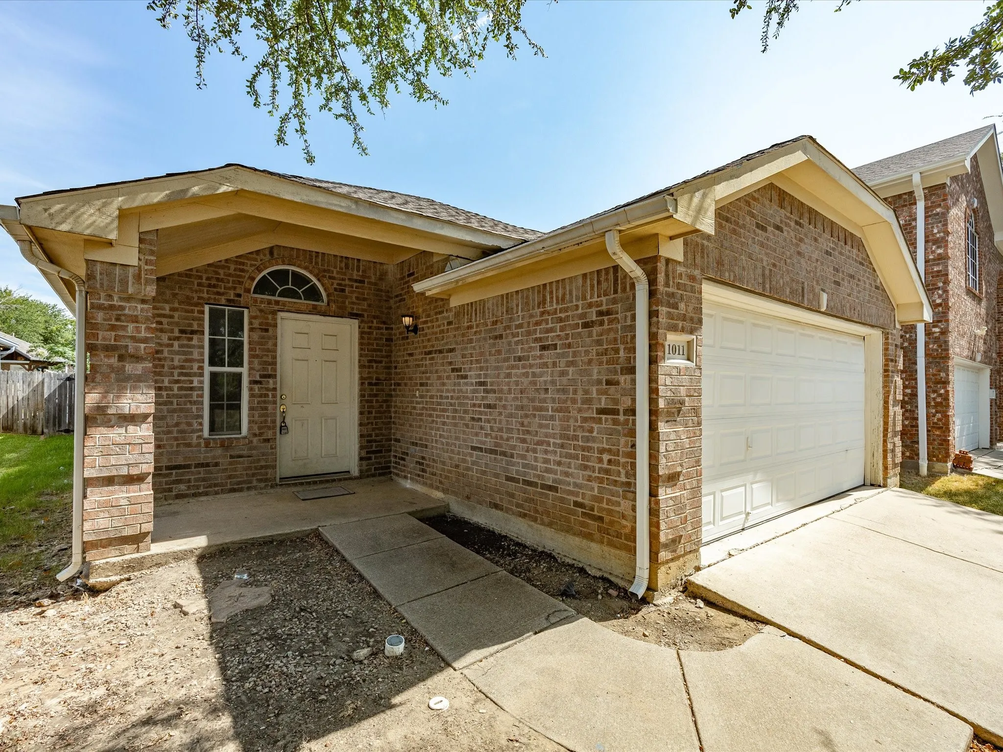 Brick facade with an arched window above the entry door, covered front porch, attached garage with a concrete driveway, and white rain gutters