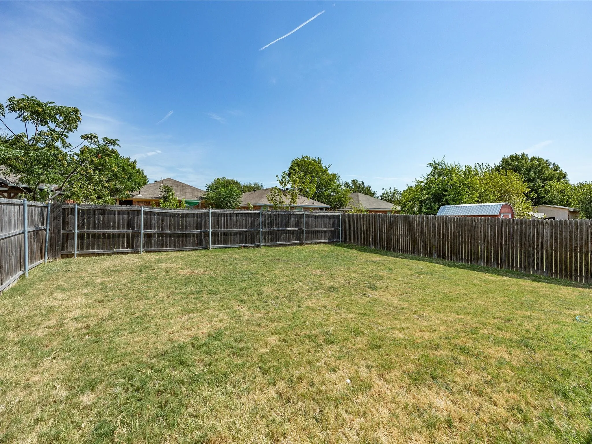 Expansive backyard featuring a wood fence, mature trees, and a storage shed