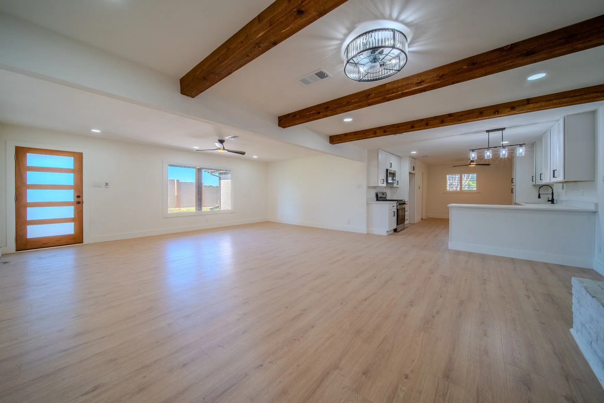 Light wood-finish flooring, exposed ceiling beams, recessed lighting, and a kitchen with white cabinetry and a breakfast bar