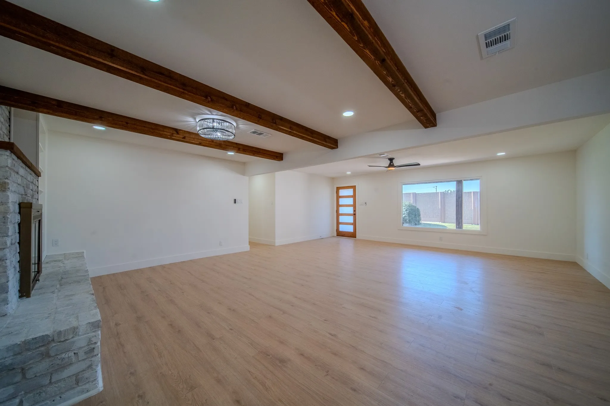 Spacious room featuring wood-finish flooring, exposed ceiling beams, a stone-clad fireplace, recessed lighting, and a contemporary ceiling fan