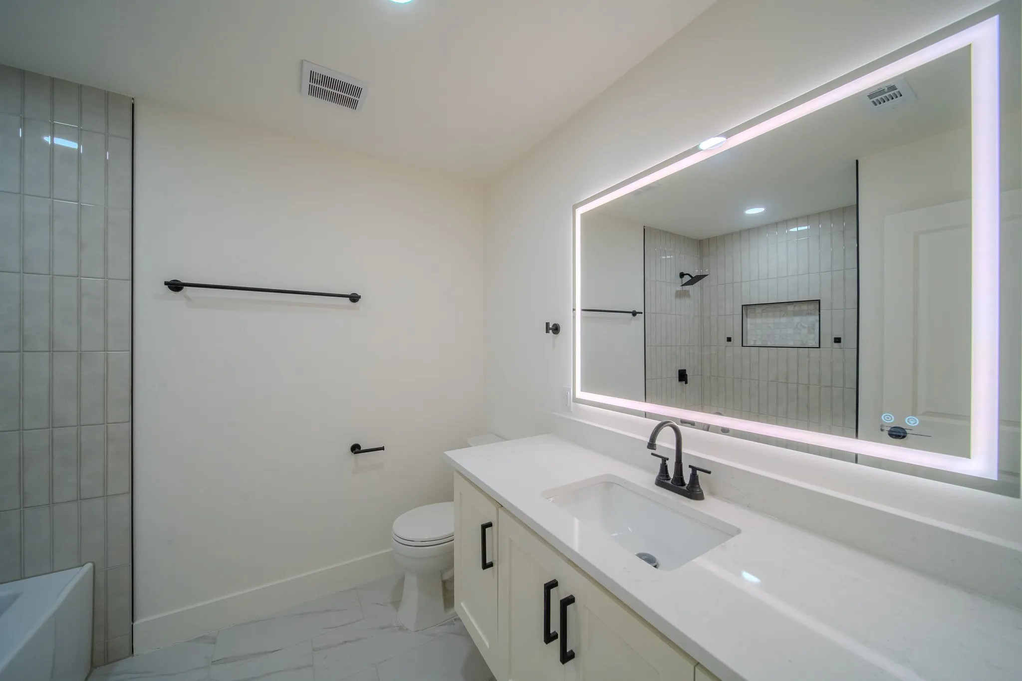 Spa-inspired primary bathroom featuring a frameless glass walk-in shower with subway tile surround, floating vanity with dual sinks and matte black hardware, LED-backlit mirror, and porcelain flooring throughout