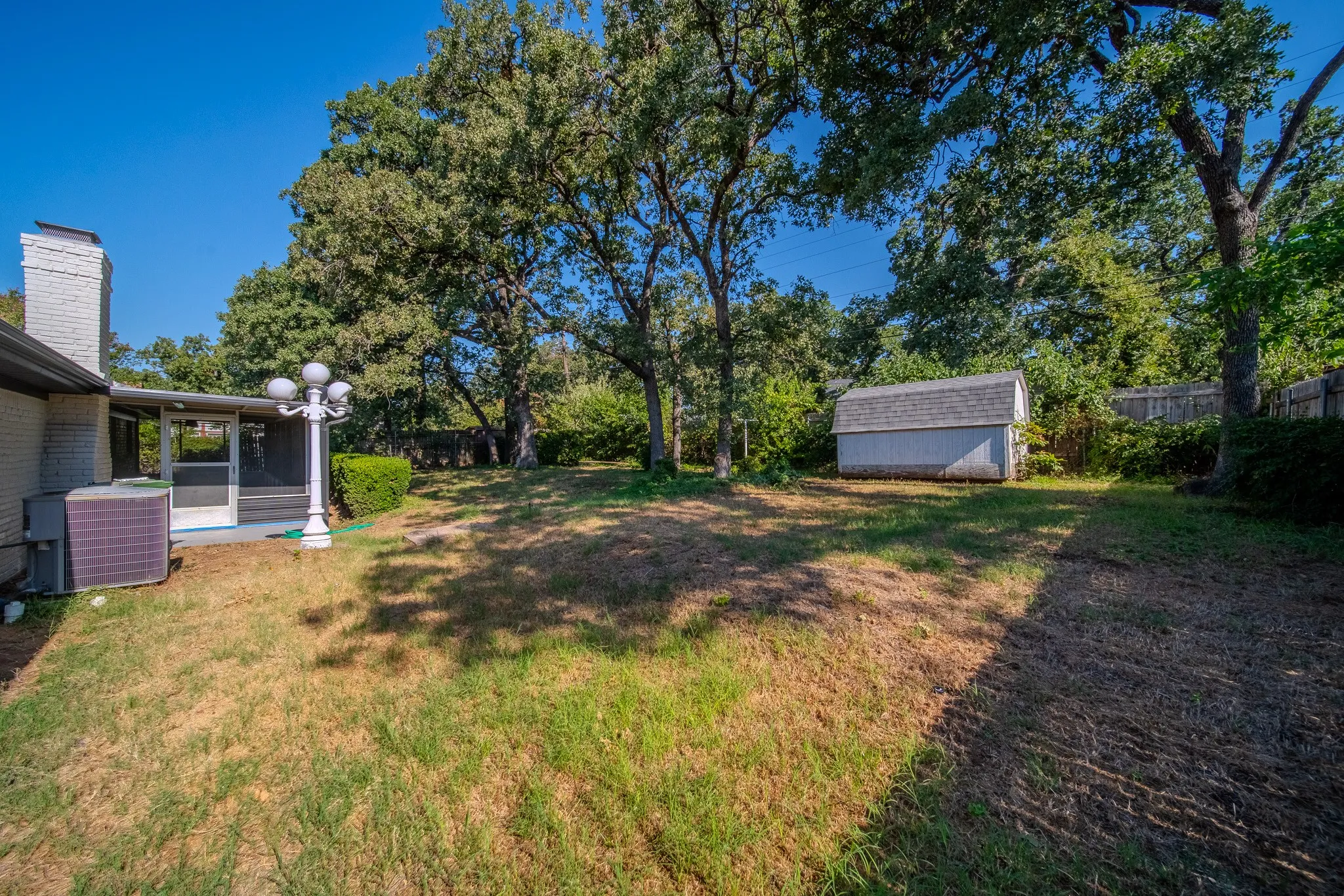 Spacious backyard featuring a screened-in patio, white brick chimney, and a separate storage shed