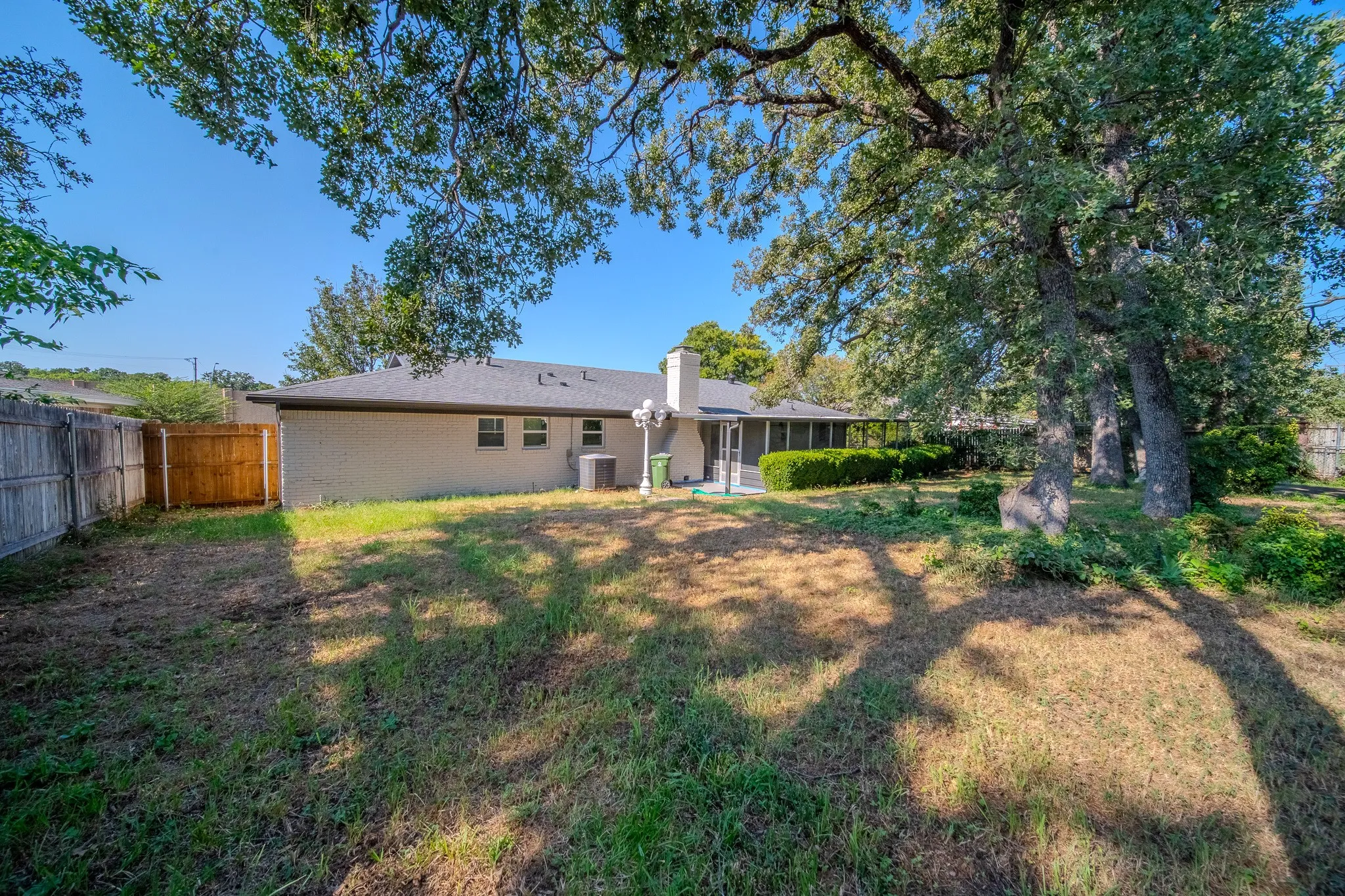 Expansive backyard with a full privacy fence, mature trees, and a screened patio