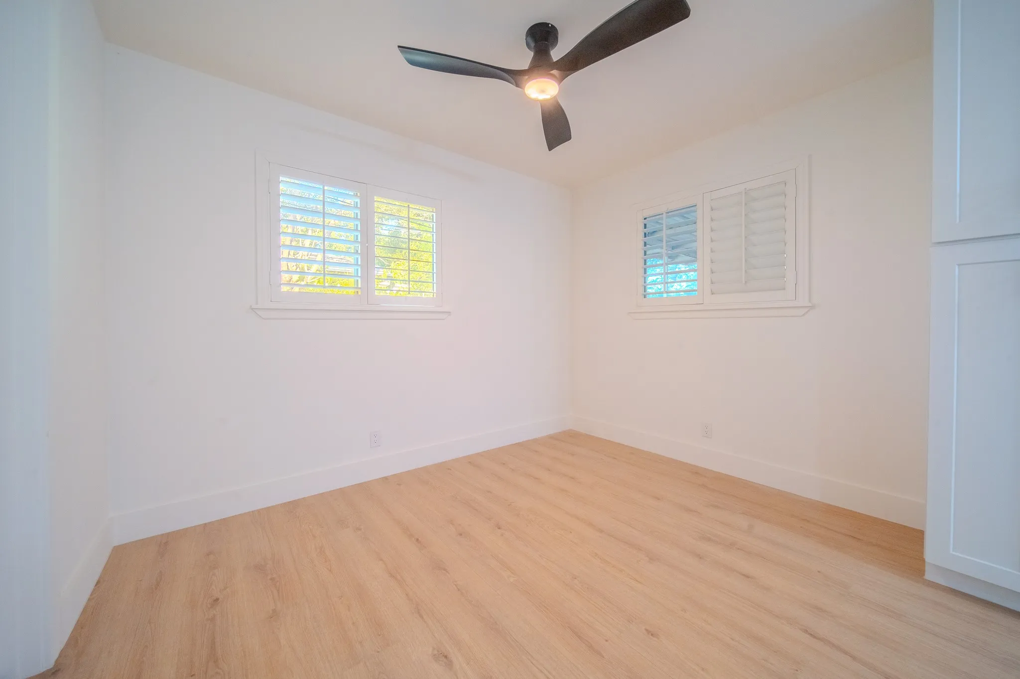 Light wood-finish flooring, white walls, and a ceiling fan with integrated lighting