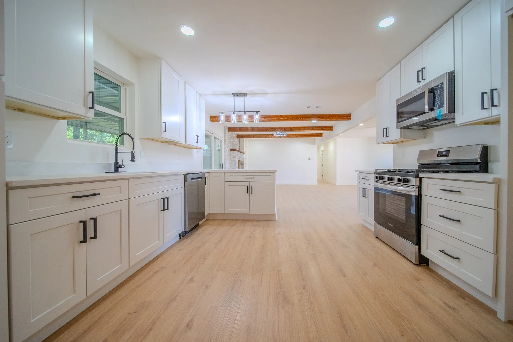 Spacious kitchen featuring white shaker cabinetry, stainless steel appliances, light wood-finish flooring, and exposed ceiling beams