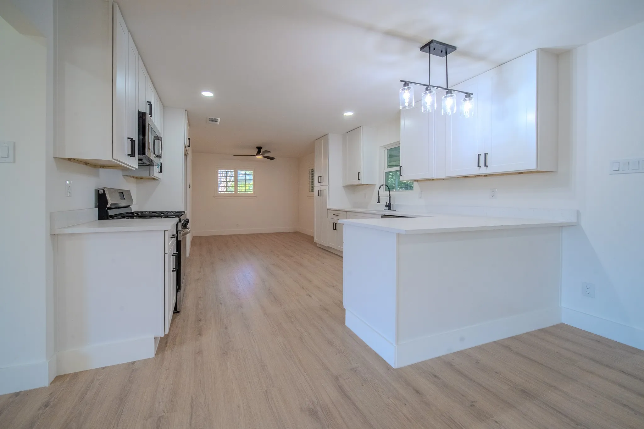Modern kitchen featuring white cabinetry, light countertops, wood-finish flooring, a stainless steel range, and an overhead microwave