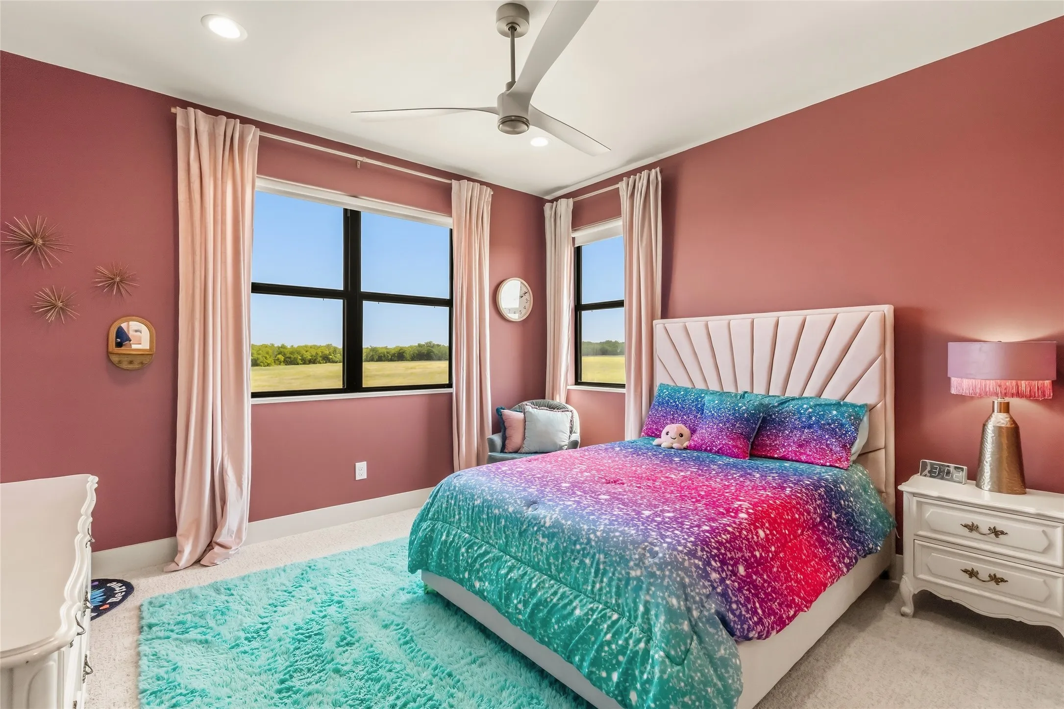 Recessed lighting, ceiling fan, large window with black framing, upholstered headboard, and light-toned carpeting