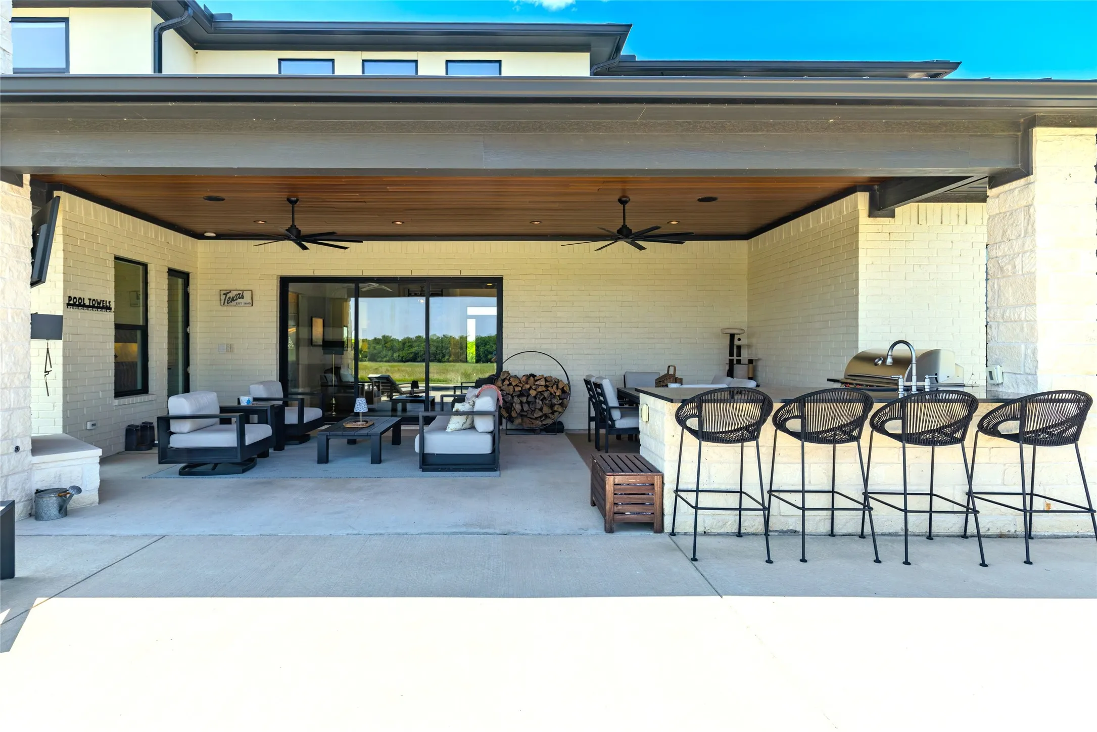 Expansive covered patio featuring a wood-finish ceiling, multiple ceiling fans, and an outdoor kitchen with a built-in grill and sink