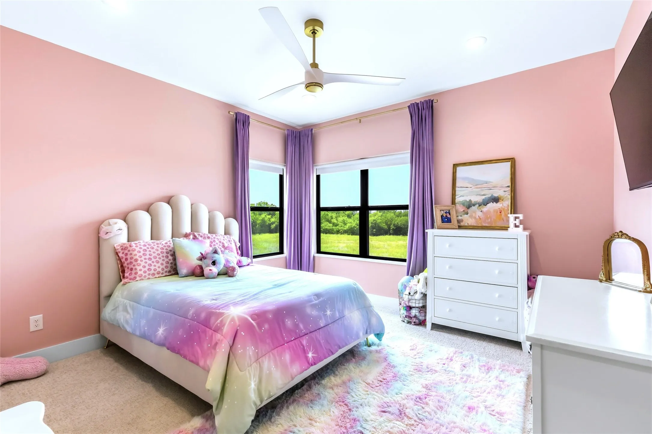 Carpeted flooring with light pink walls, featuring windows with purple drapes, and a ceiling fan with gold-tone accents