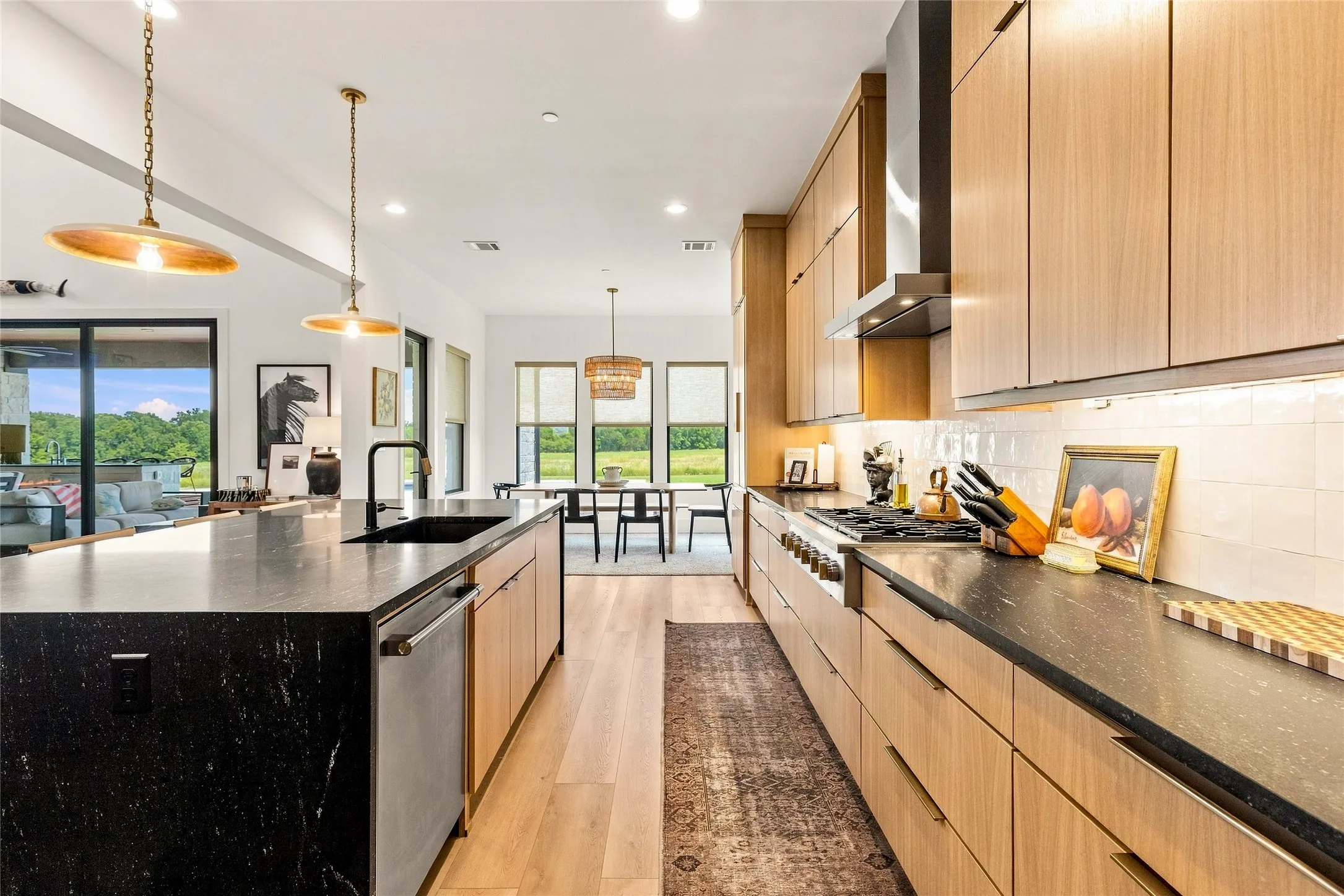 Open-concept kitchen featuring an expansive island with a built-in sink, rift-sawn white oak cabinetry, stainless steel  Monogram appliances and a seconod dining area