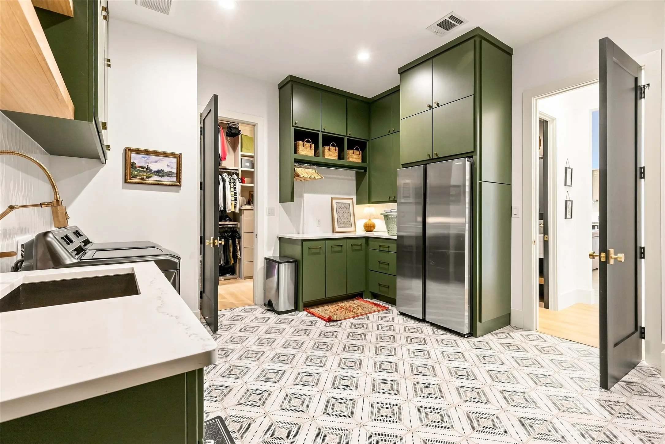 Custom green cabinetry, patterned tile flooring, built-in stainless steel refrigerator, white quartz countertops, and a utility sink