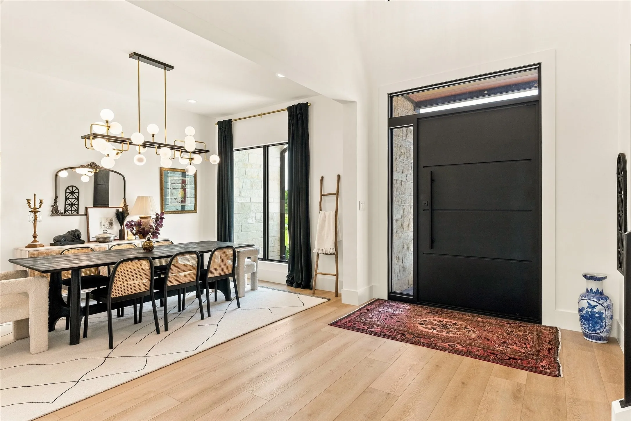 Light LVP flooring, a modern black entry door with transom and sidelight, and a two-story ceiling.  Dining room adjoins with kitchen with a bar in between