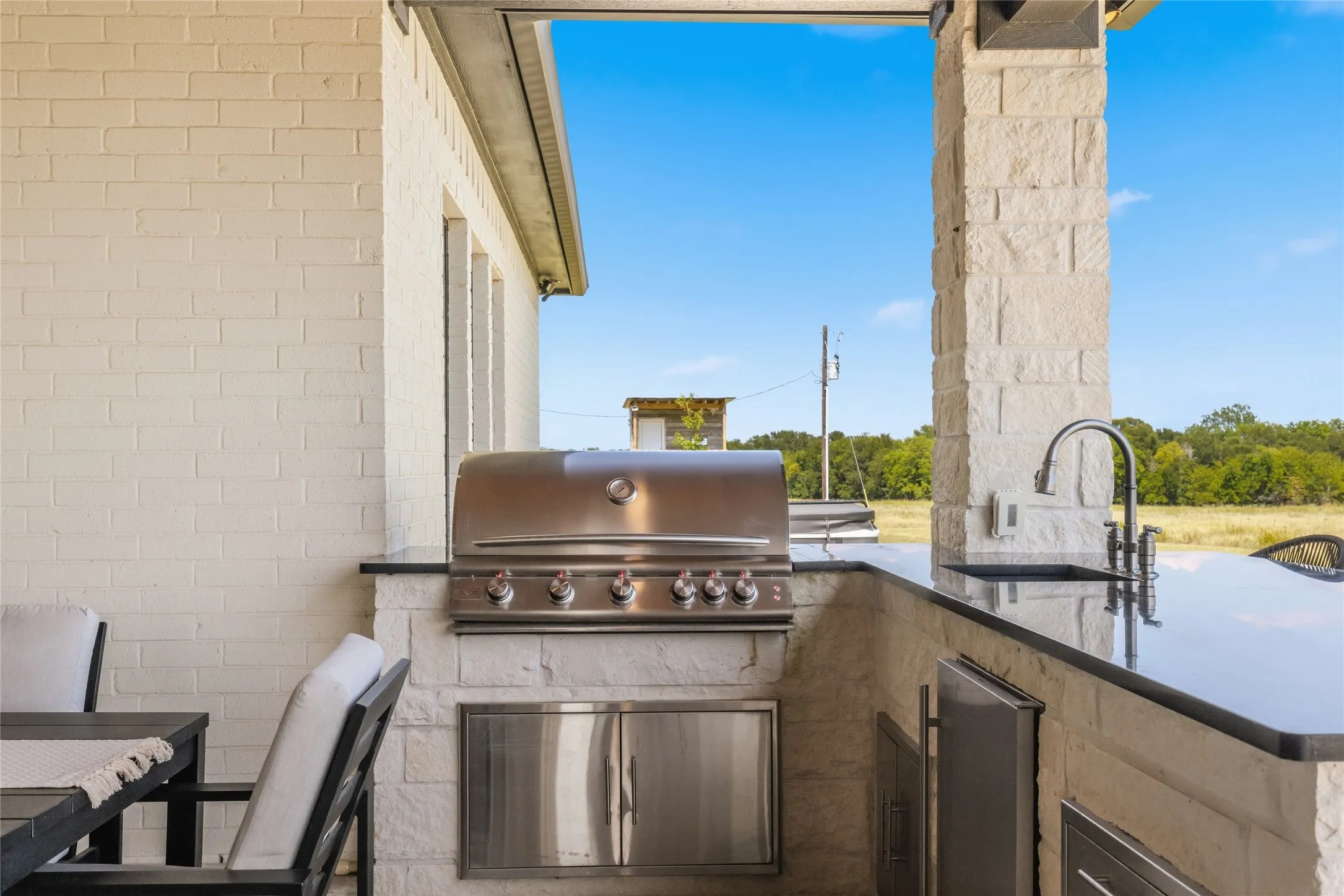 Outdoor kitchen featuring a built-in stainless steel grill, integrated sink, and dark countertops