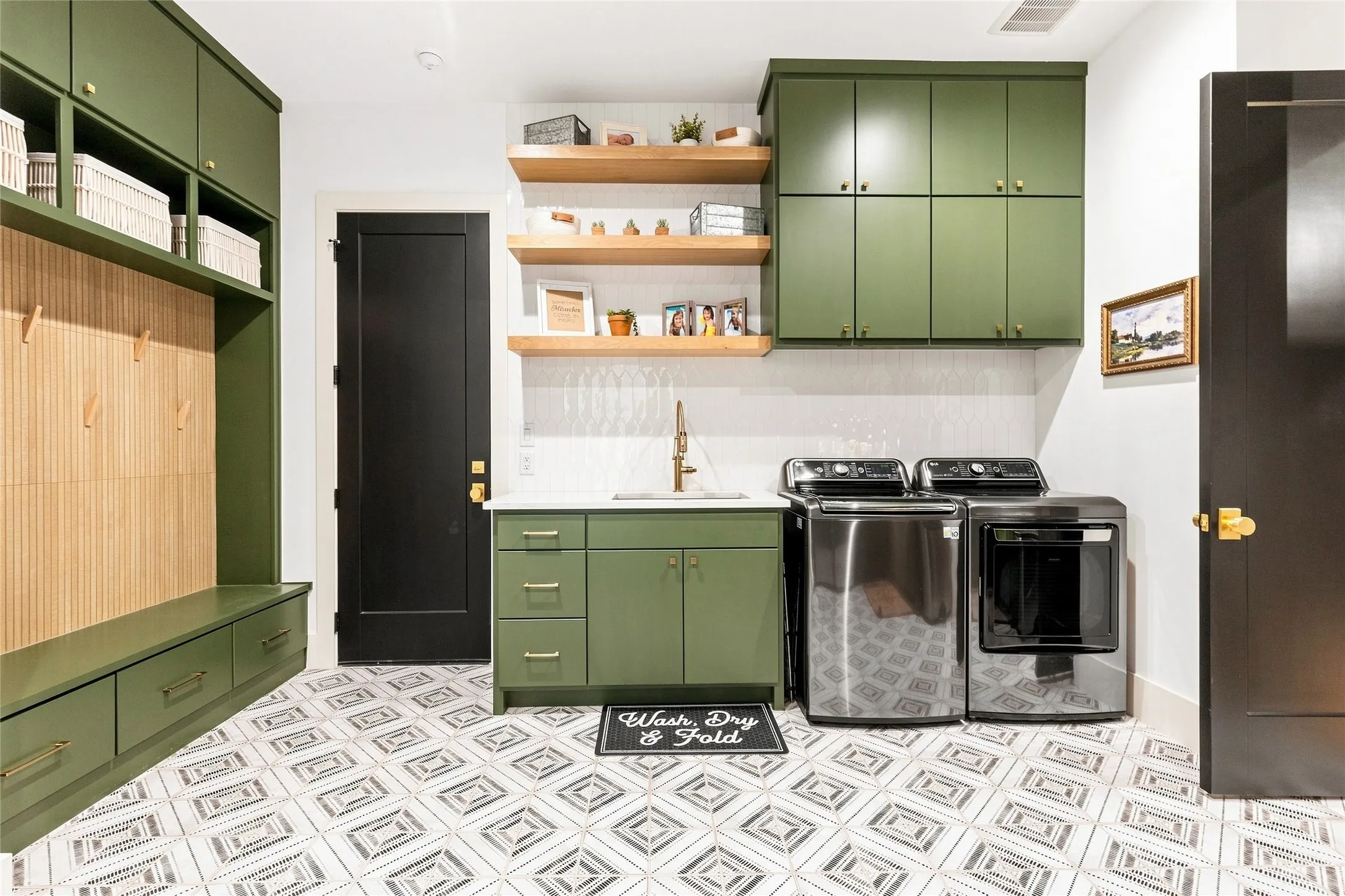 Green cabinetry, white oak open shelving, white quartz countertop with sink, patterned tile flooring, and integrated mudroom-style storage with bench seating
