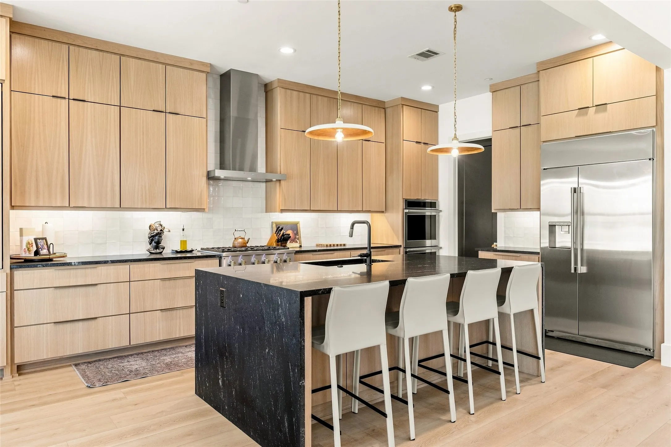 Kitchen featuring rift-sawn white oak cabinetry, dark granite countertops, stainless steel Monogram appliances, a center island with seating, and pendant lighting