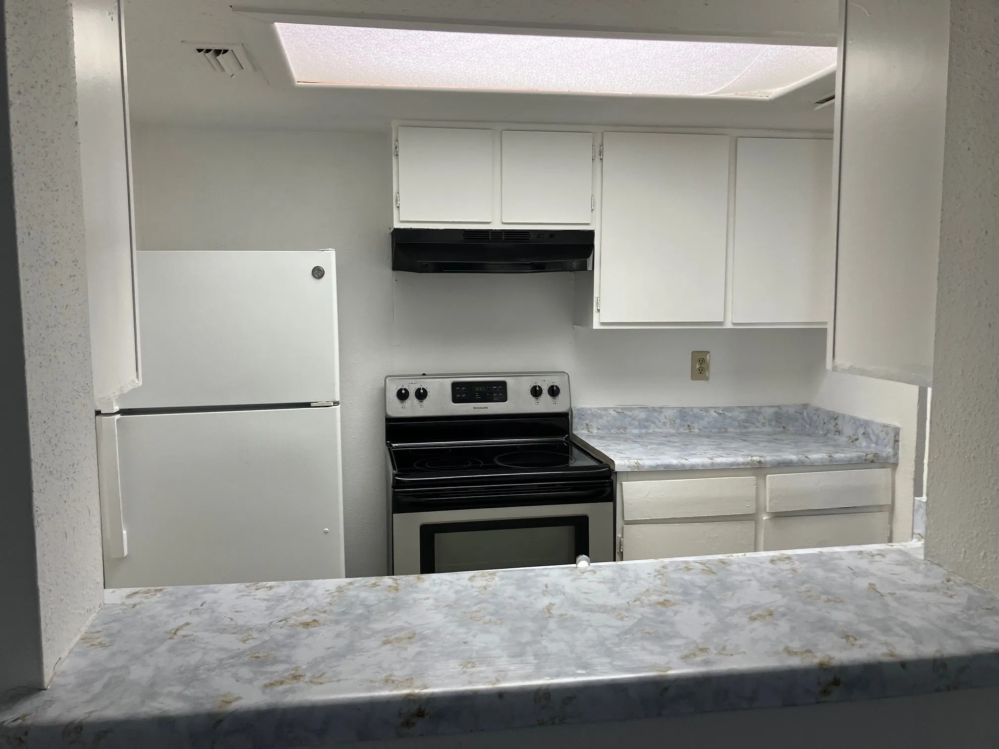 White upper and lower cabinetry, patterned countertops, and a built-in range with an overhead exhaust fan